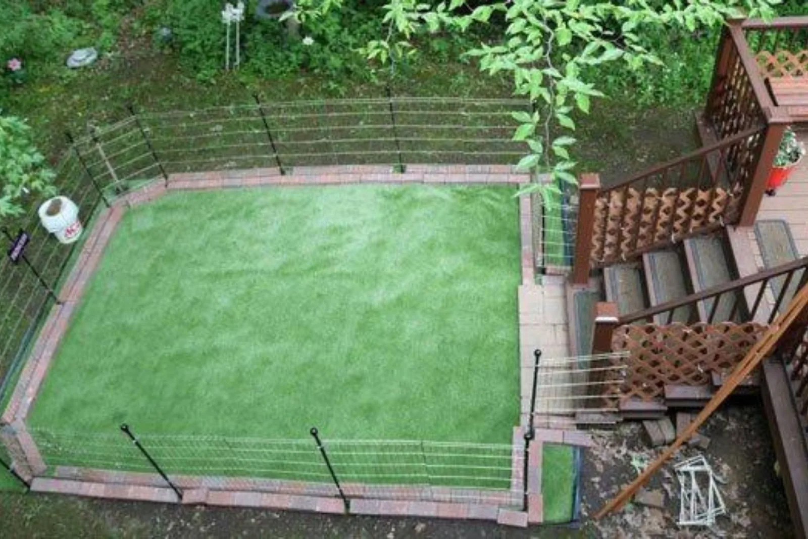 Artificial turf or fake grass creates a low-maintenance, clean, and pet-friendly dog run in a fenced-in backyard with a deck and steps.