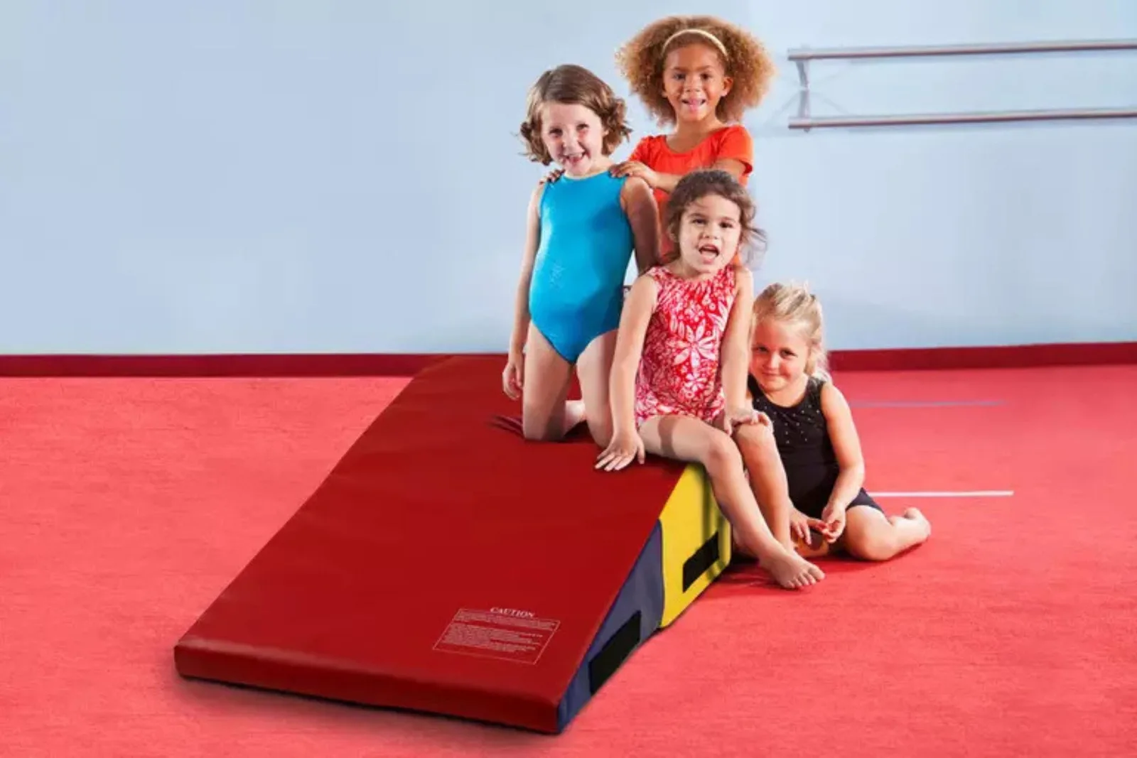 Cheese wedge mat or folding incline mat in red and yellow provides a cushioned learning tool for children practicing basic gymnastics and tumbling skills.