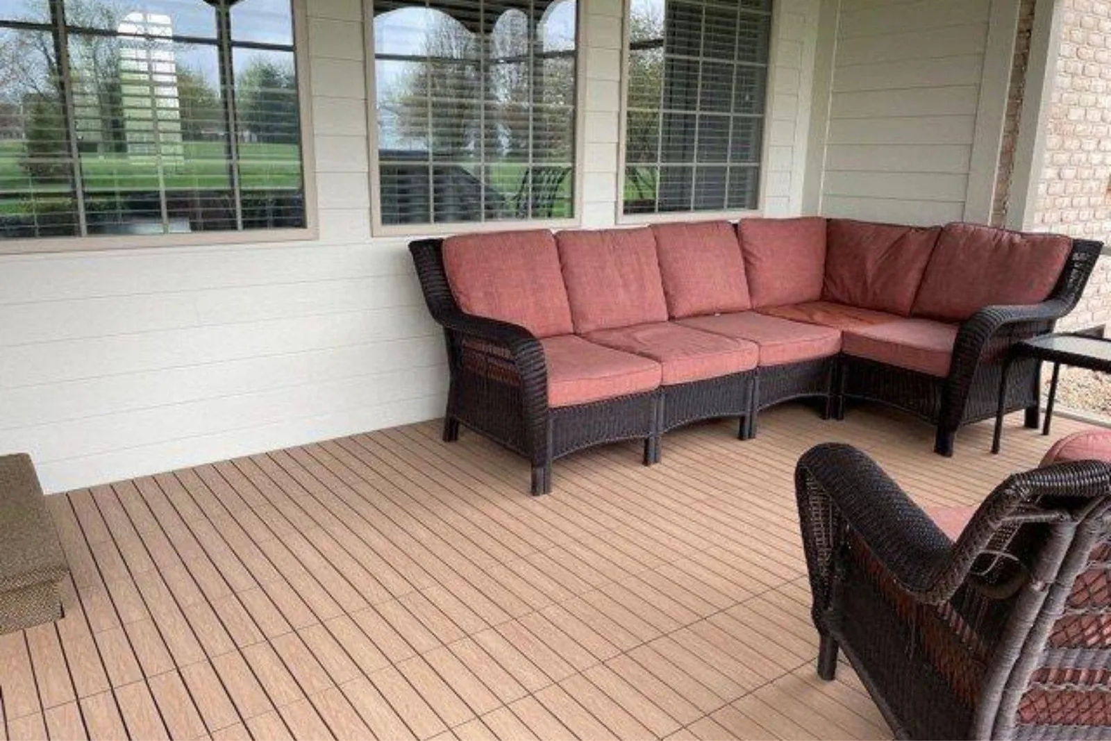 Composite deck tiles in a light wood grain finish, creating a comfortable and low-maintenance outdoor flooring solution on a covered porch with wicker furniture.