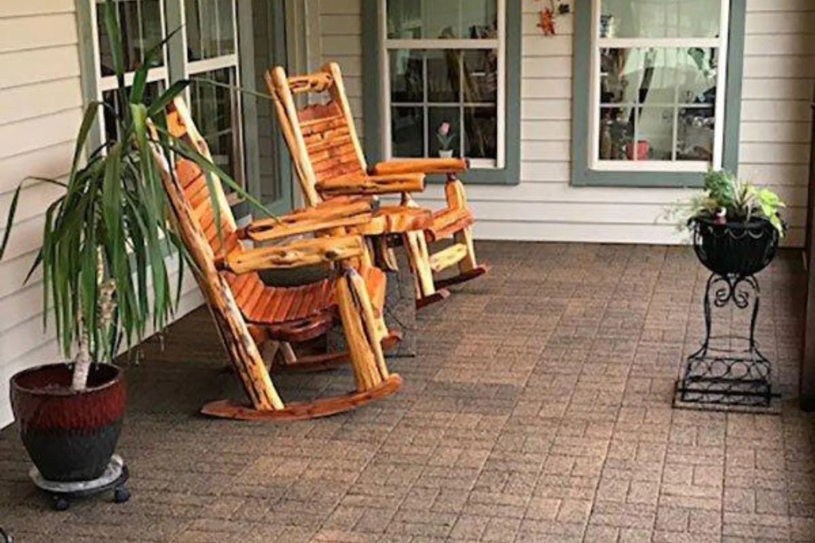 Alt Text: Flagstone rubber pavers in a rustic brown color provide a durable and cushioned outdoor flooring solution for a covered porch with wooden rocking chairs and potted plants.
