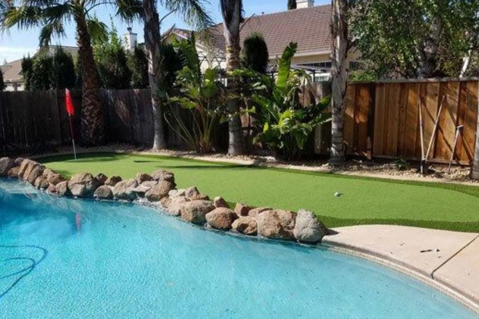 Putting green turf provides a low-maintenance and professional-looking surface for a backyard golf green, with a small ball visible near the edge of a swimming pool.