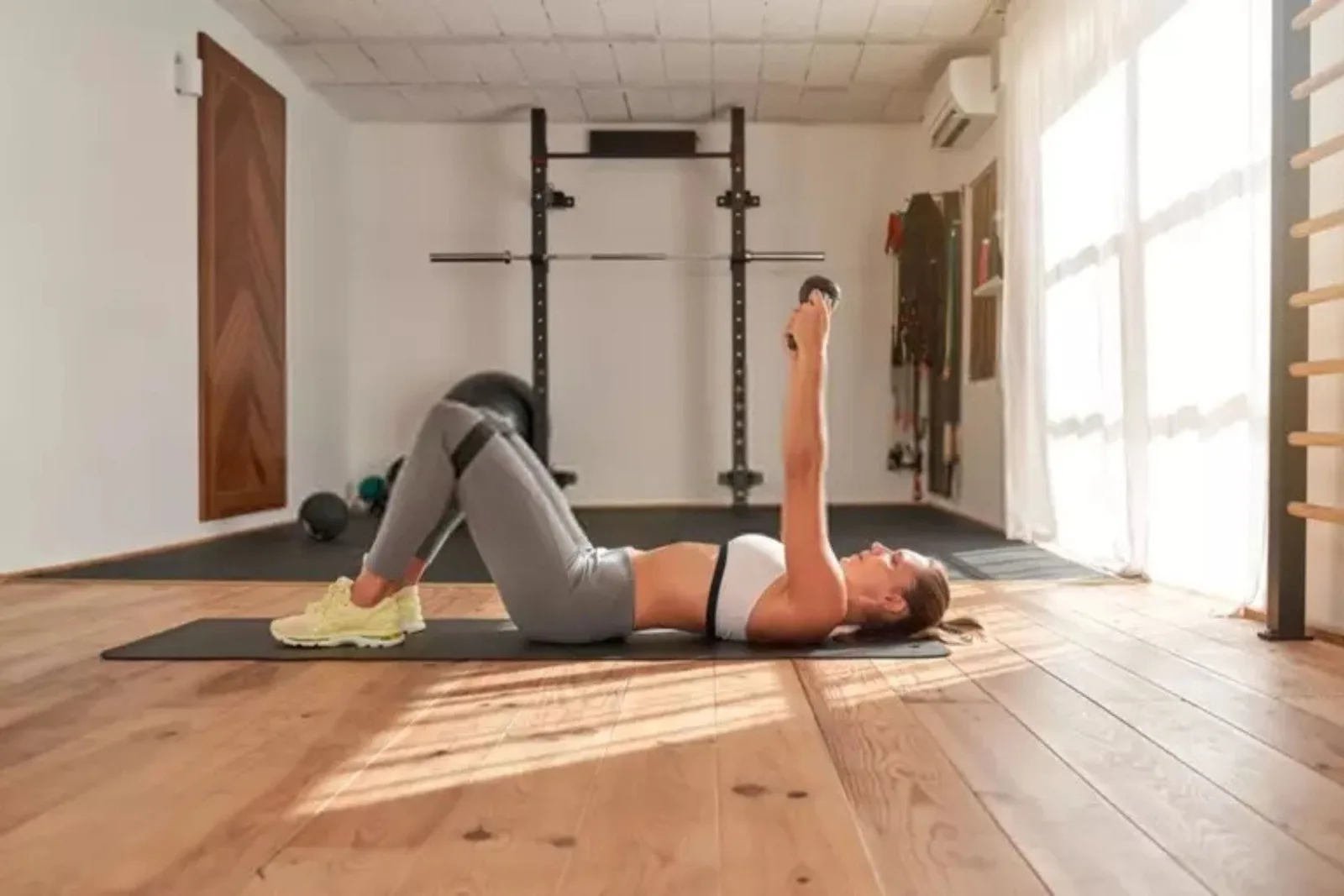Person doing a dumbbell press on a durable black foam mat on top of light wood flooring, a high-quality and protective flooring solution for a home gym.