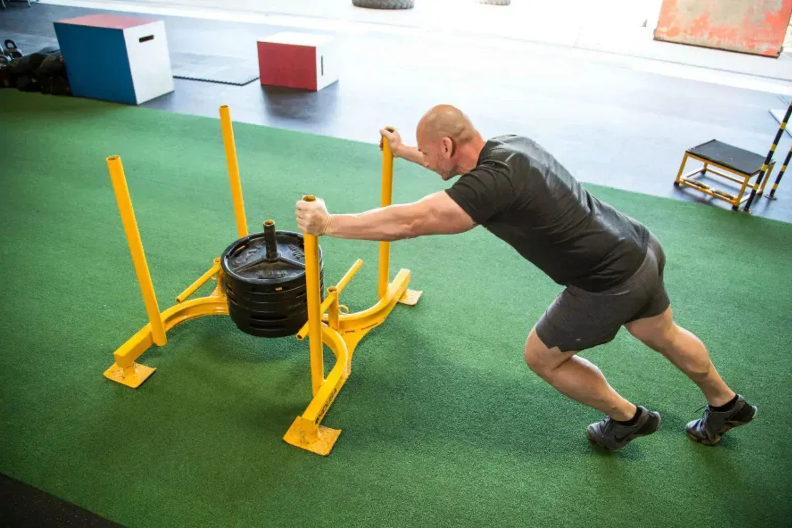 Person doing a sled push on durable green artificial turf, a high-performance and long-lasting flooring solution for a gym or athletic training space.
