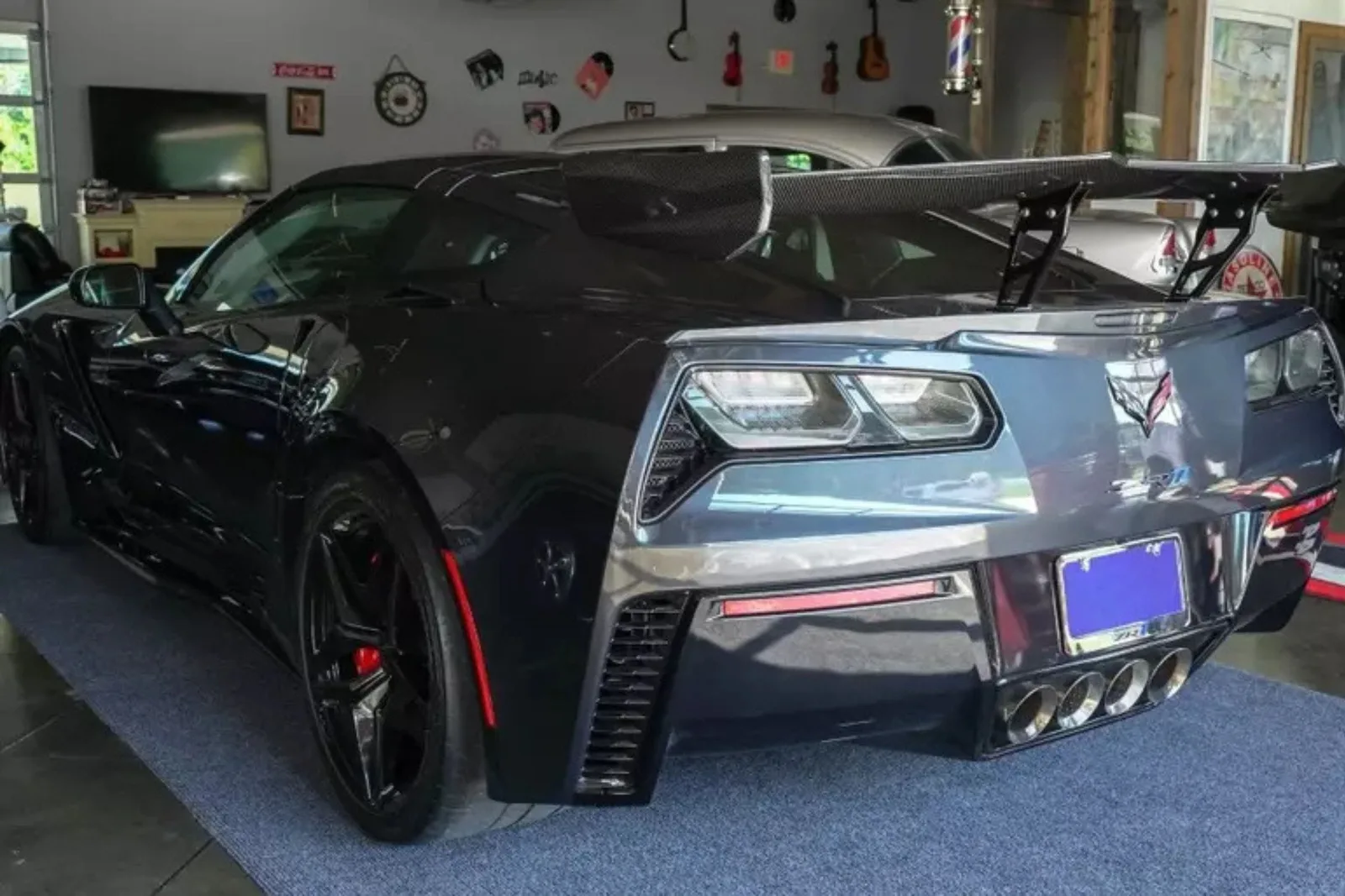 The rear of a black sports car is parked in a garage on carpet garage flooring. The durable roll-out garage mat protects the floor from vehicle fluids and tire marks, while also providing a sleek, professional look.