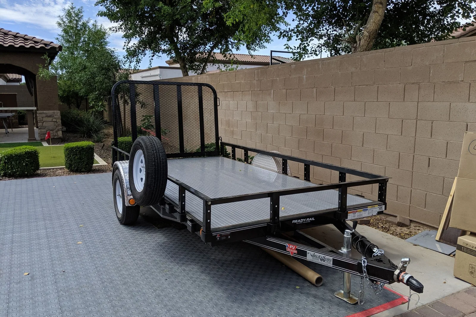 A utility trailer is parked on gray interlocking garage floor tiles with a non-slip diamond-plate pattern. The durable garage tiles provide a protective, clean, and stable surface for vehicle parking and equipment storage.