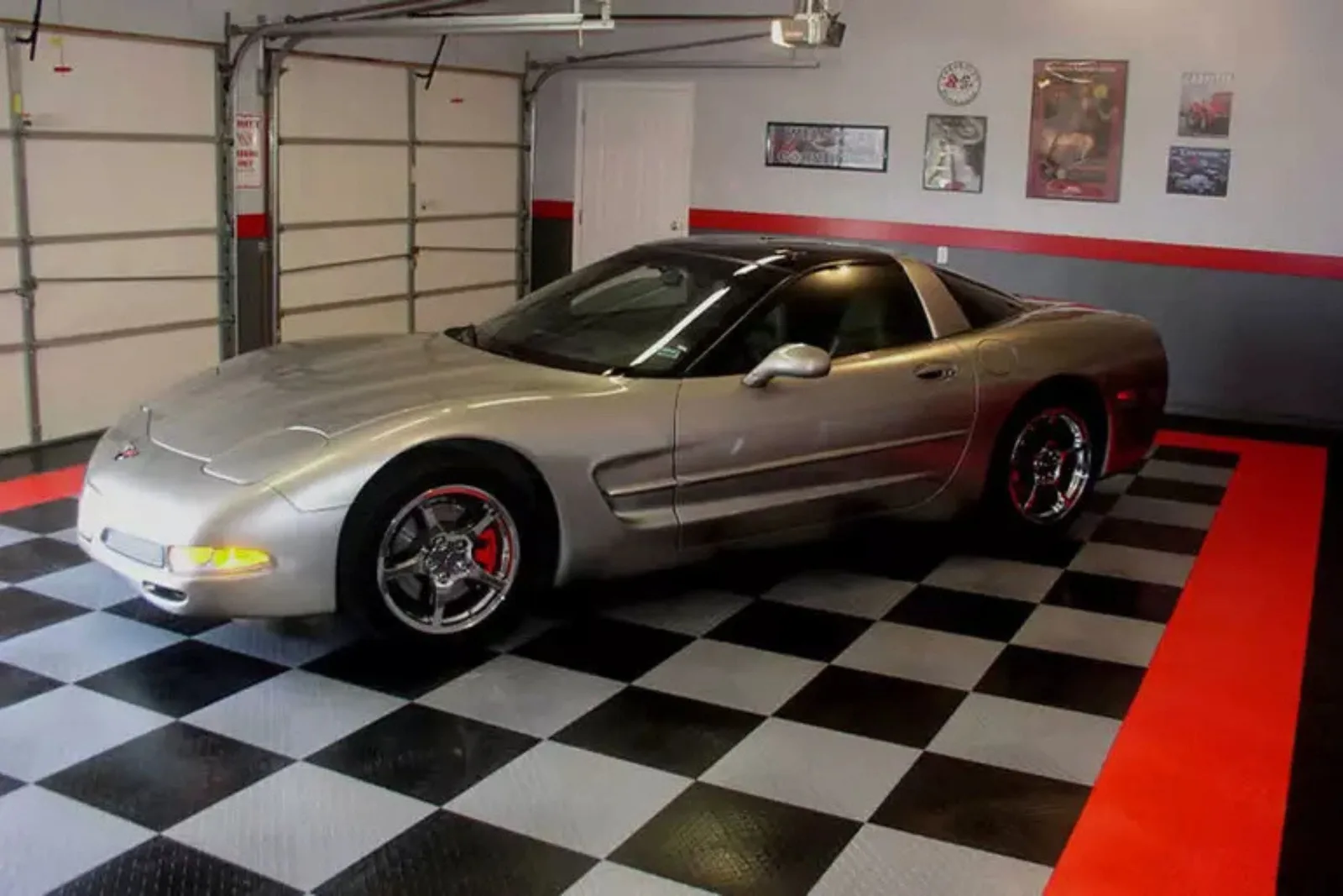 silver Chevrolet Corvette is parked on a custom checkerboard interlocking garage floor. The durable garage tiles in black, white, and red create a striking, classic racing look that's perfect for a showroom or car enthusiast's garage.