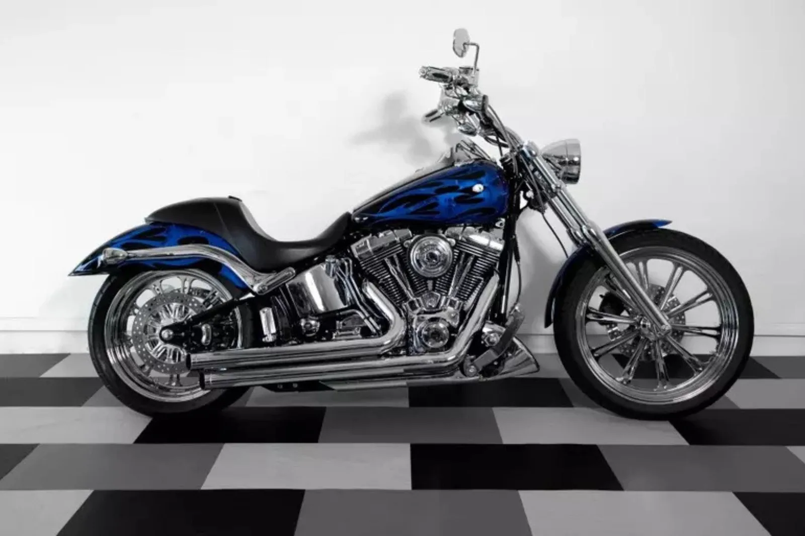 A custom blue and black motorcycle with chrome details is parked on a black and white checkerboard garage floor. The interlocking garage tiles provide a durable, stylish, and easy-to-clean surface for displaying vehicles in a showroom or garage.
