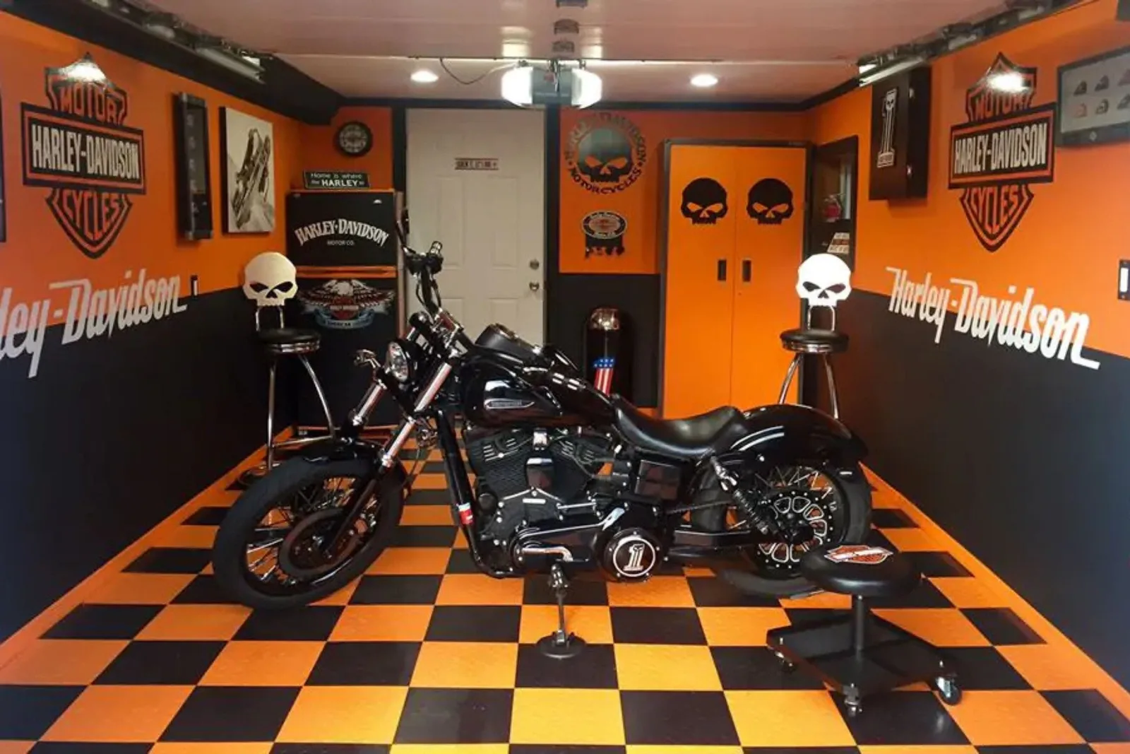 A motorcycle is parked on a custom orange and black checkerboard garage floor. The interlocking garage tiles complement the Harley-Davidson themed decor, providing a durable and stylish surface for this highly customized garage or showroom.
