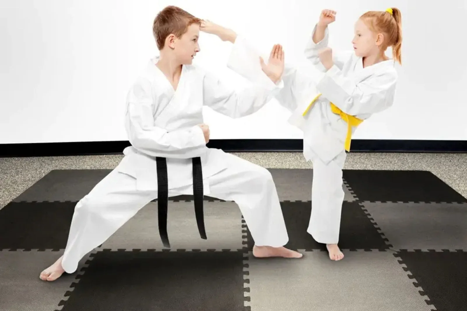 Interlocking foam tiles or martial arts mat in black and gray create a safe, shock-absorbent training surface for two children practicing karate and Taekwondo.