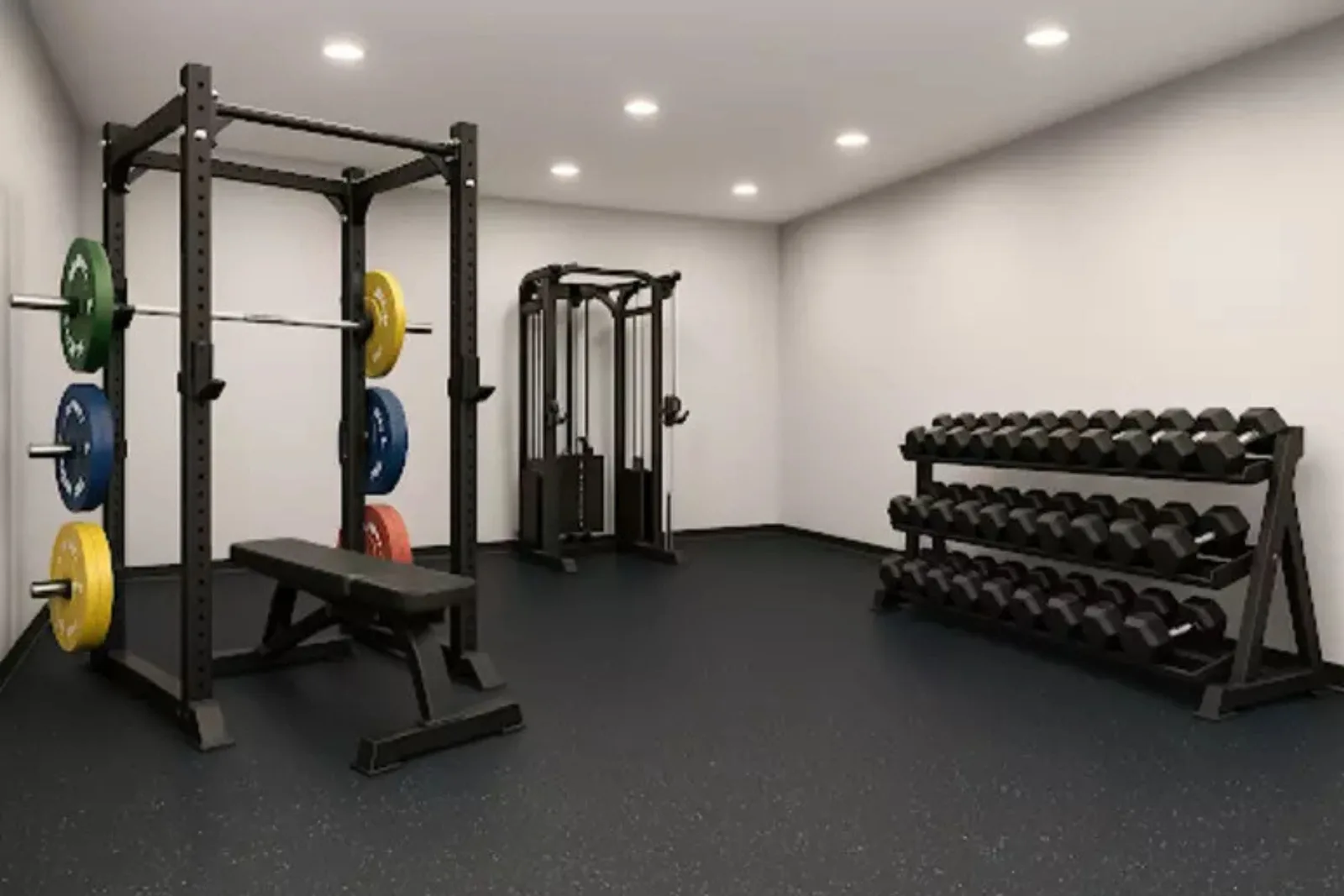 A clean, modern gym facility featuring a continuous black rubber gym floor. The durable rubber matting provides a protective and stable surface for a squat rack with colored plates, a cable machine, and a three-tier dumbbell rack.