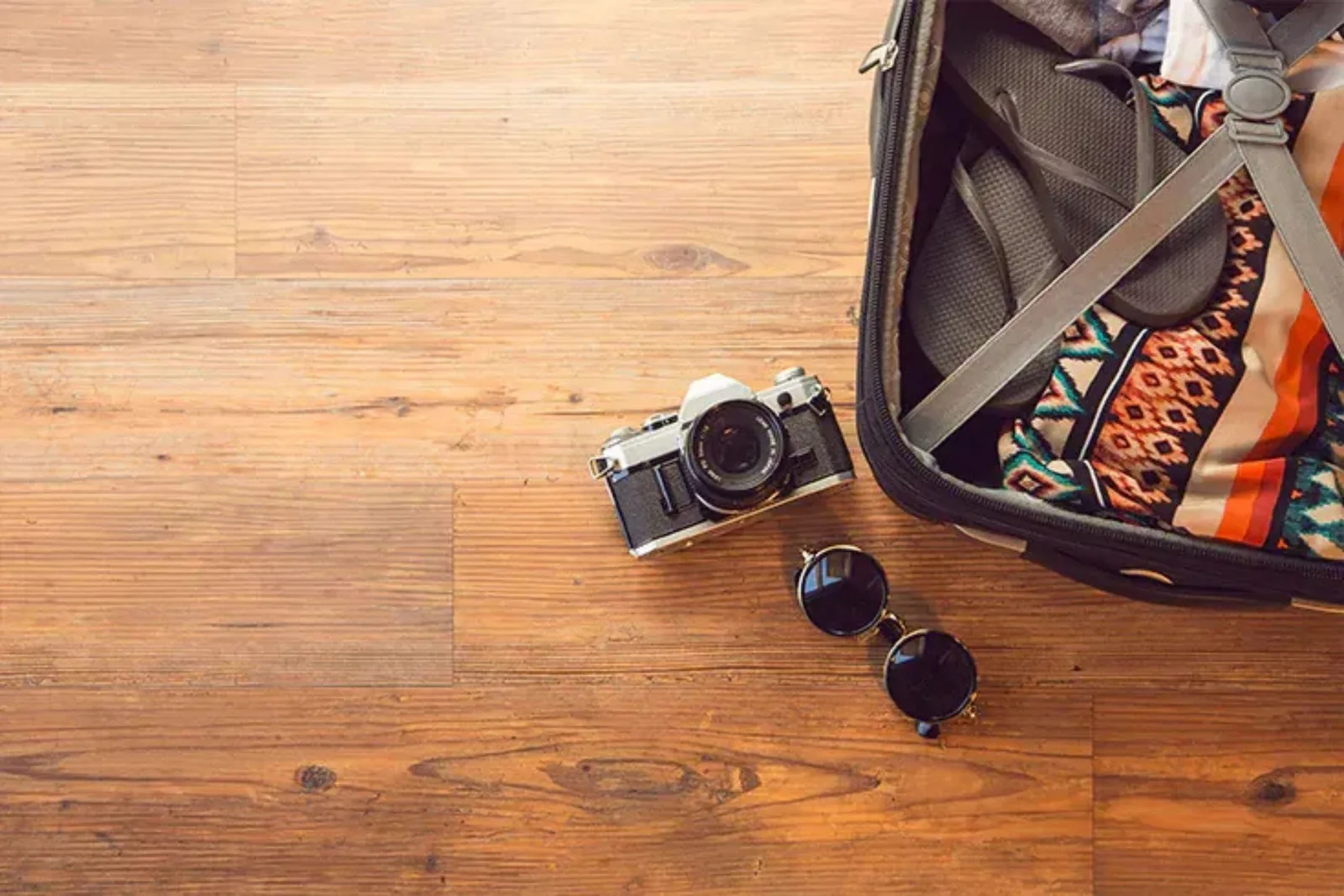 Overhead view of a camera and sunglasses on durable light brown wood-look vinyl plank flooring, a low-maintenance and water-resistant alternative to hardwood.