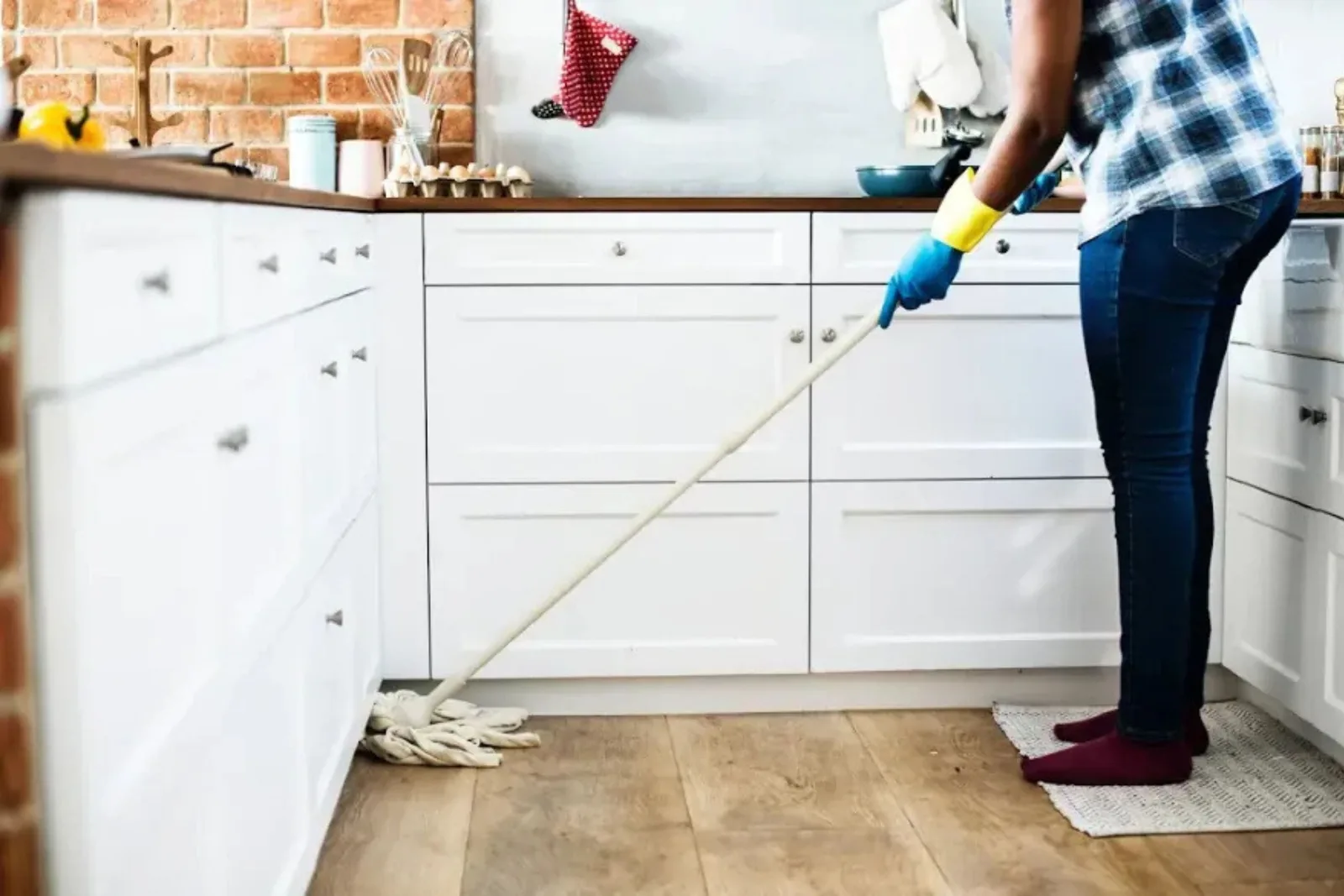 Person mopping a kitchen with durable medium wood-look vinyl plank flooring, a water-resistant and easy-to-clean alternative to hardwood.