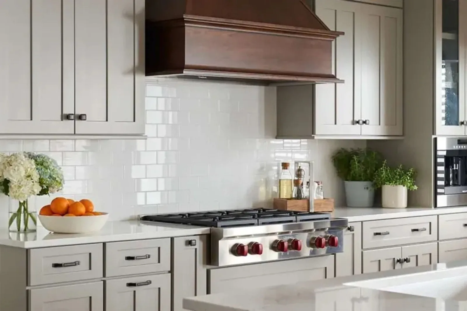 Modern kitchen with a gray-brown wood range hood above a stainless steel stove with red knobs and a white subway tile backsplash.
