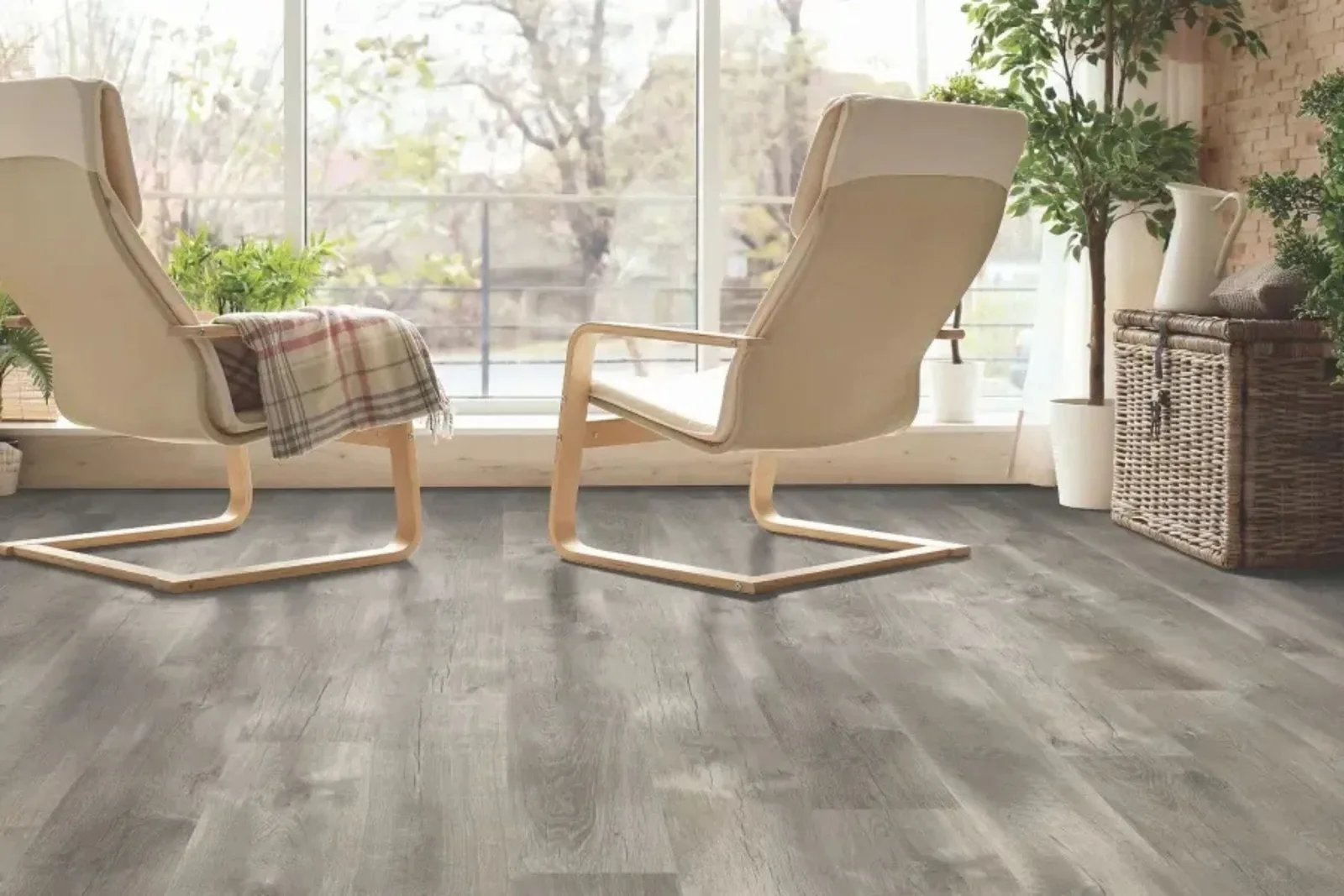 A bright, sunlit room with two modern lounge chairs, featuring gray wood-look vinyl plank flooring. The durable, waterproof residential flooring provides an attractive and easy-to-clean surface, ideal for living areas or sunrooms.