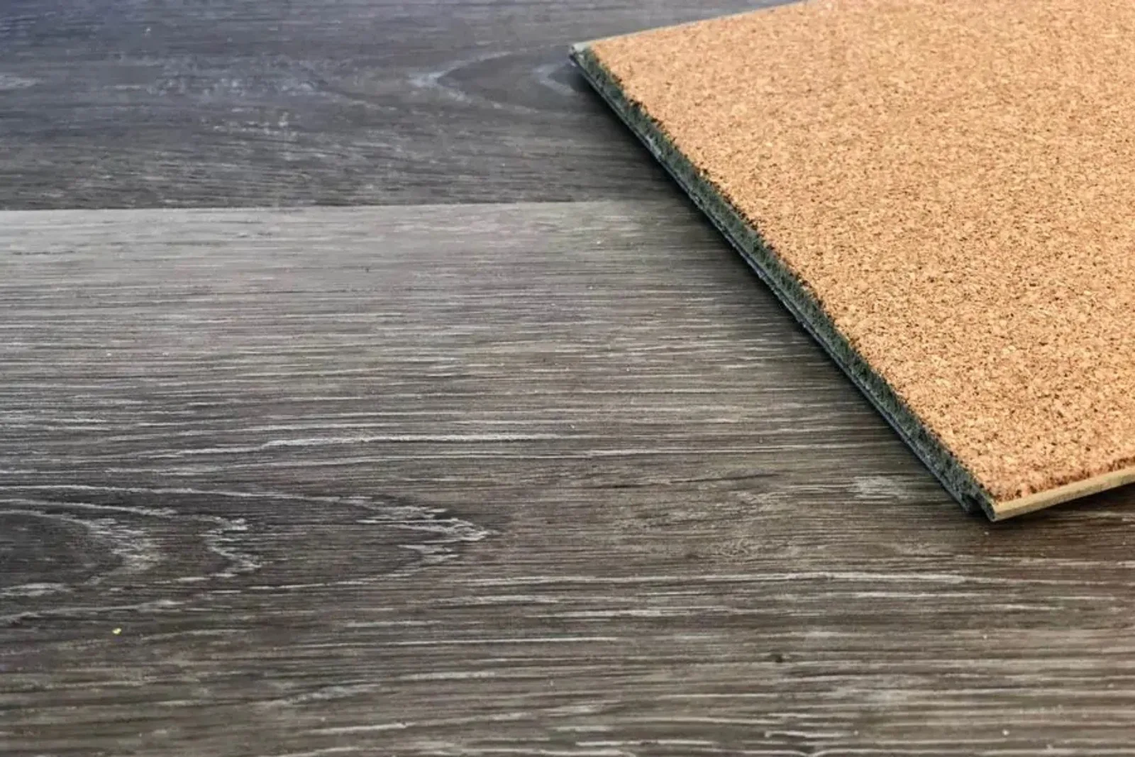 Close-up of a durable gray wood-look vinyl plank flooring with an attached cork underlayment, a water-resistant and sound-absorbing flooring solution.
