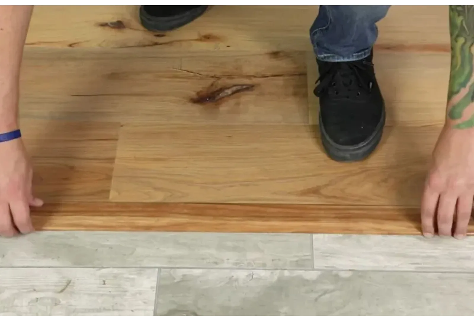 Person installing a durable wood-look vinyl T-molding transition piece between wood-look and tile-look vinyl flooring.