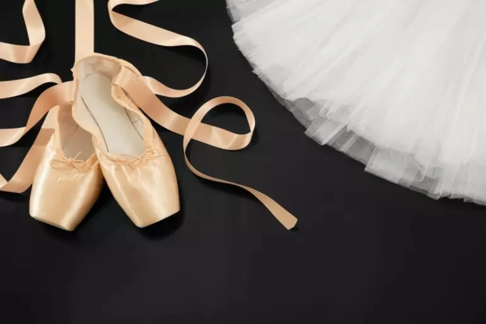 Ballet shoes and white tutu on black dance floor rolls.