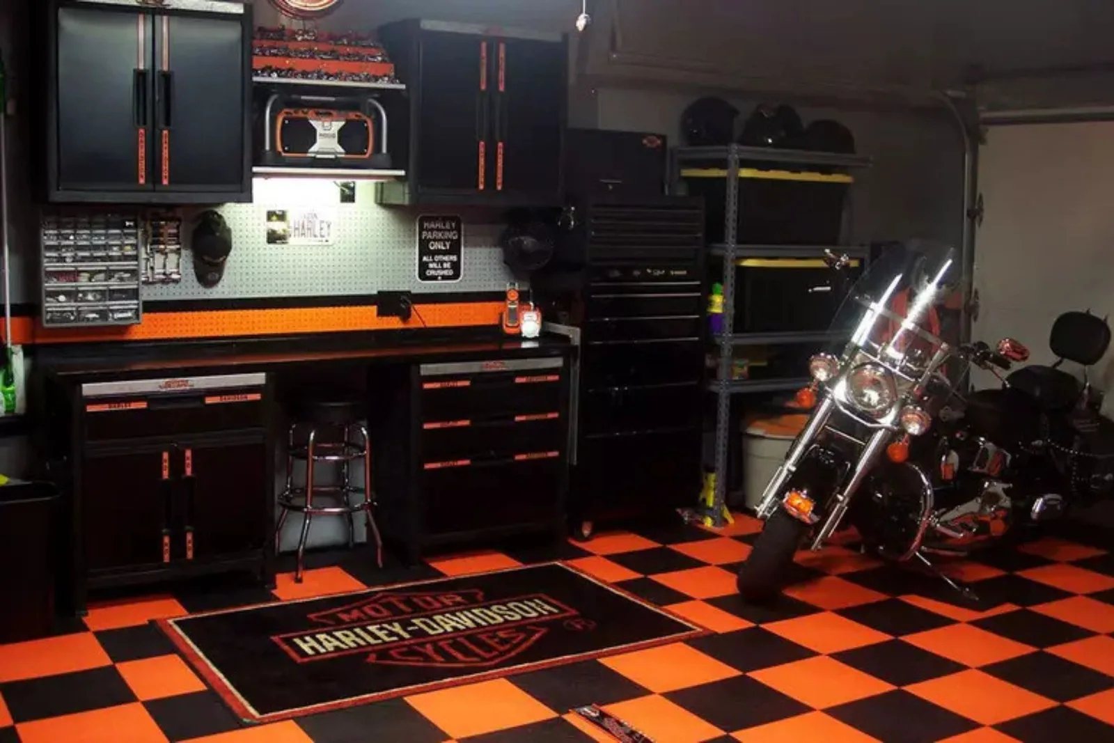 A highly customized garage and workshop featuring orange and black checkerboard interlocking garage tiles. The durable garage flooring complements the black and orange cabinetry and provides a protective, stylish base for a parked motorcycle and a Harley