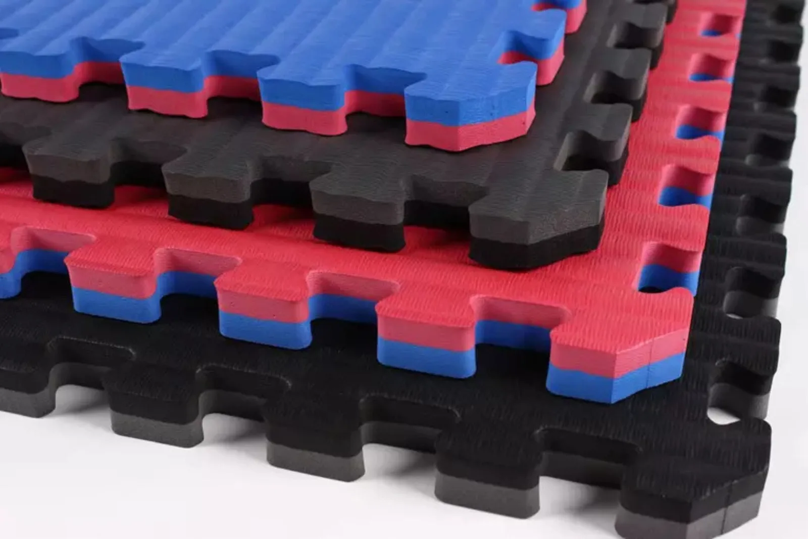 A stack of colorful, thick foam interlocking tiles with distinct red, blue, and black layers. These shock-absorbent foam mats are designed for martial arts, MMA, and cheerleading, providing maximum safety and comfort for high-impact activities.