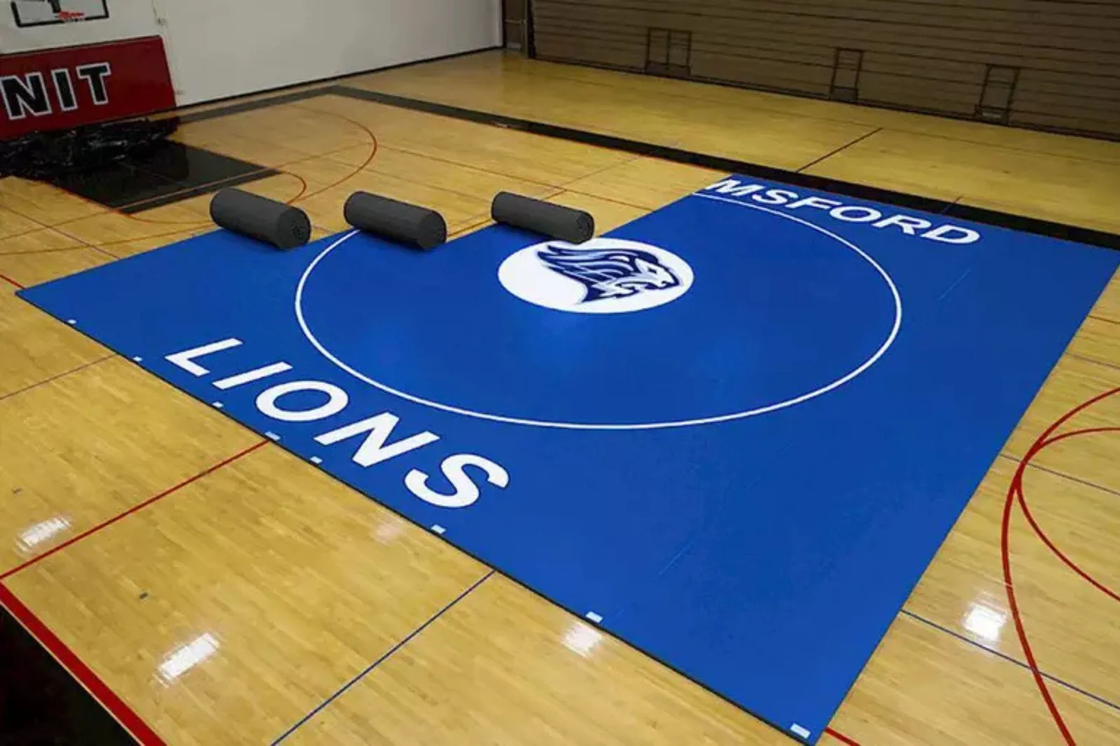 Indoor gymnasium with durable blue wrestling mats featuring a white lion logo, a high-performance and protective flooring solution for athletics.