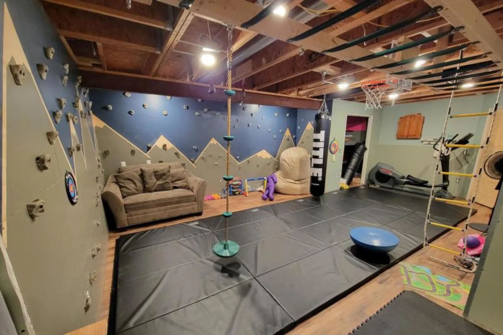 Home gym with durable black foam floor mats and a climbing wall, providing a high-performance and protective flooring solution for an active residential space.