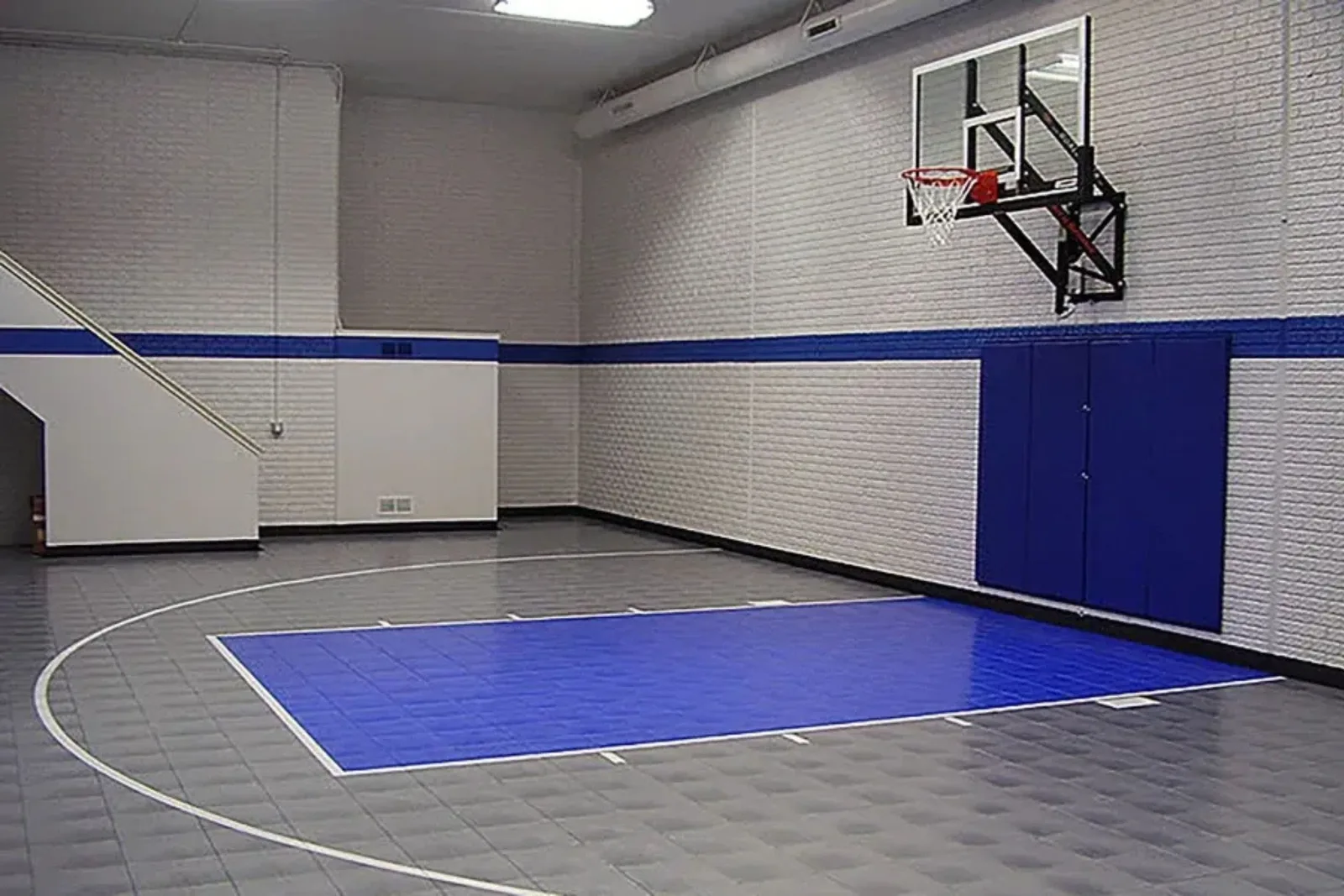 Indoor home gym with a basketball court featuring durable gray and blue plastic sports tiles, a professional and high-performance flooring solution.