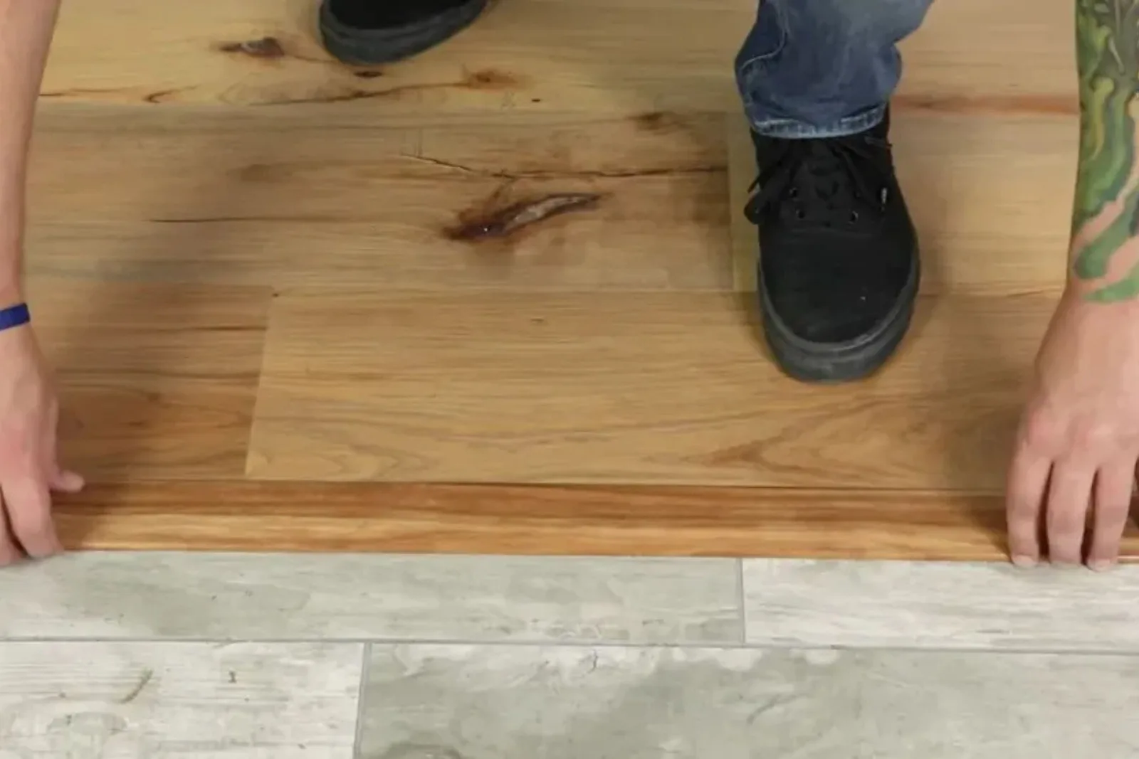 Person installing a durable wood-look vinyl T-molding transition piece between wood-look and tile-look vinyl flooring.
