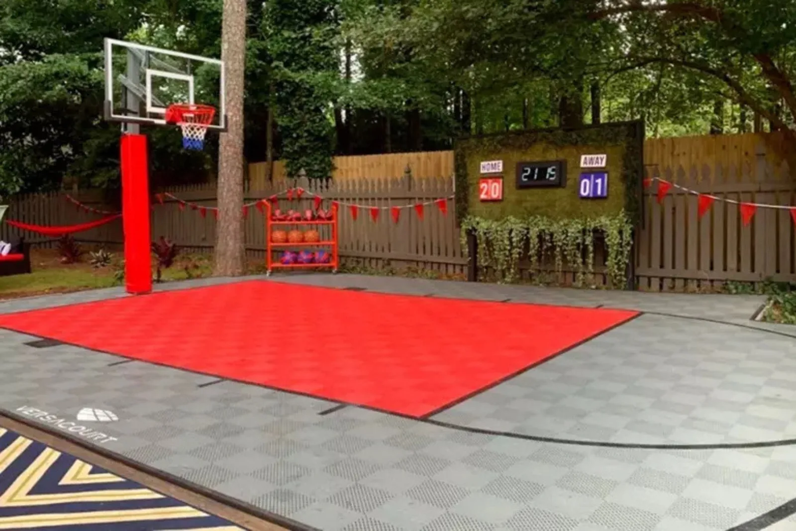 A backyard basketball court featuring interlocking court tiles for sports in a custom design. The court includes a central red key section surrounded by gray and black tiles, providing a durable, all-weather, and low-maintenance surface for basketball.