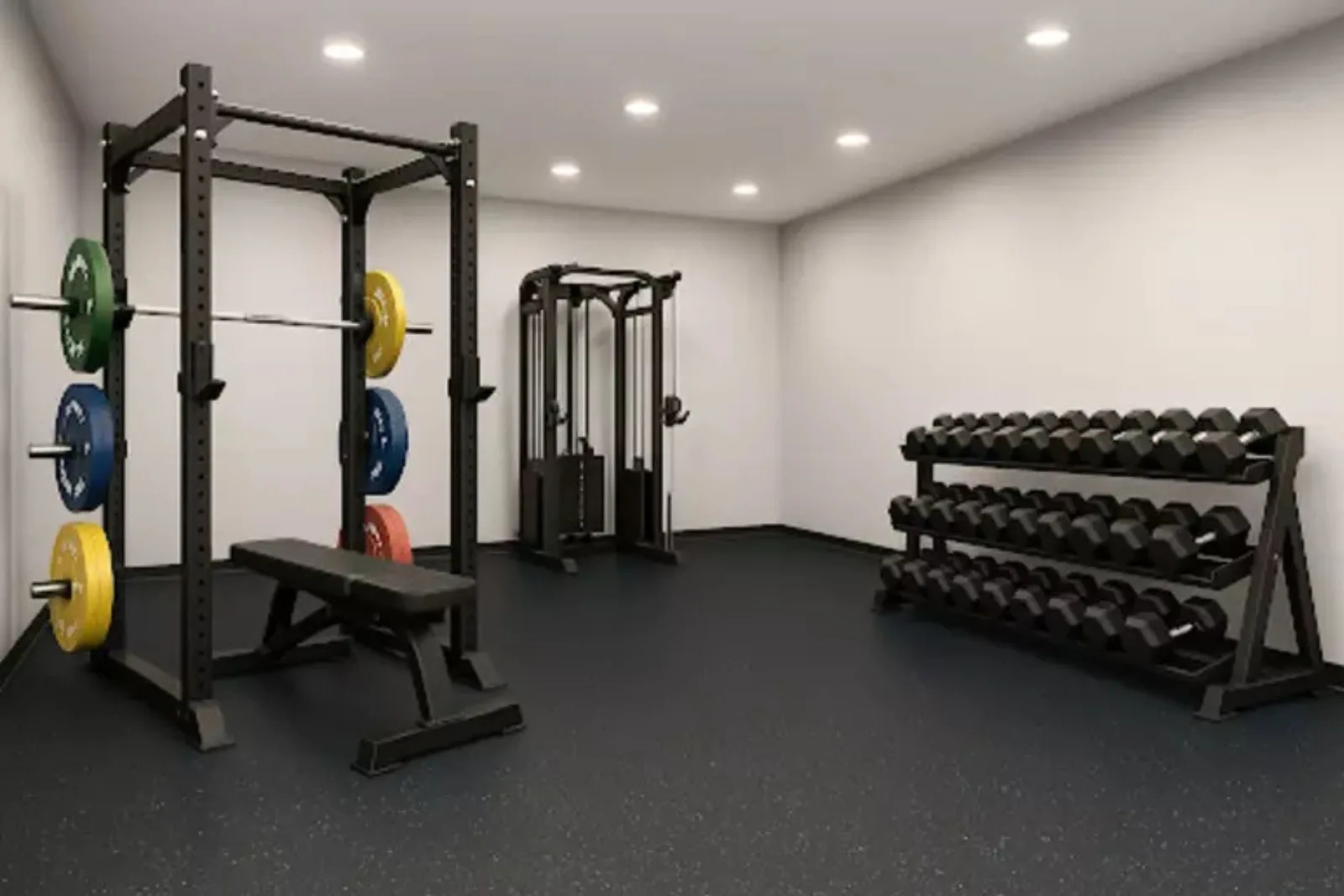 A clean, brightly lit commercial or home gym facility featuring a continuous black speckled rubber gym floor. The durable rubber matting provides a protective and stable surface for a power rack, cable machine, and a large three-tier dumbbell rack.
