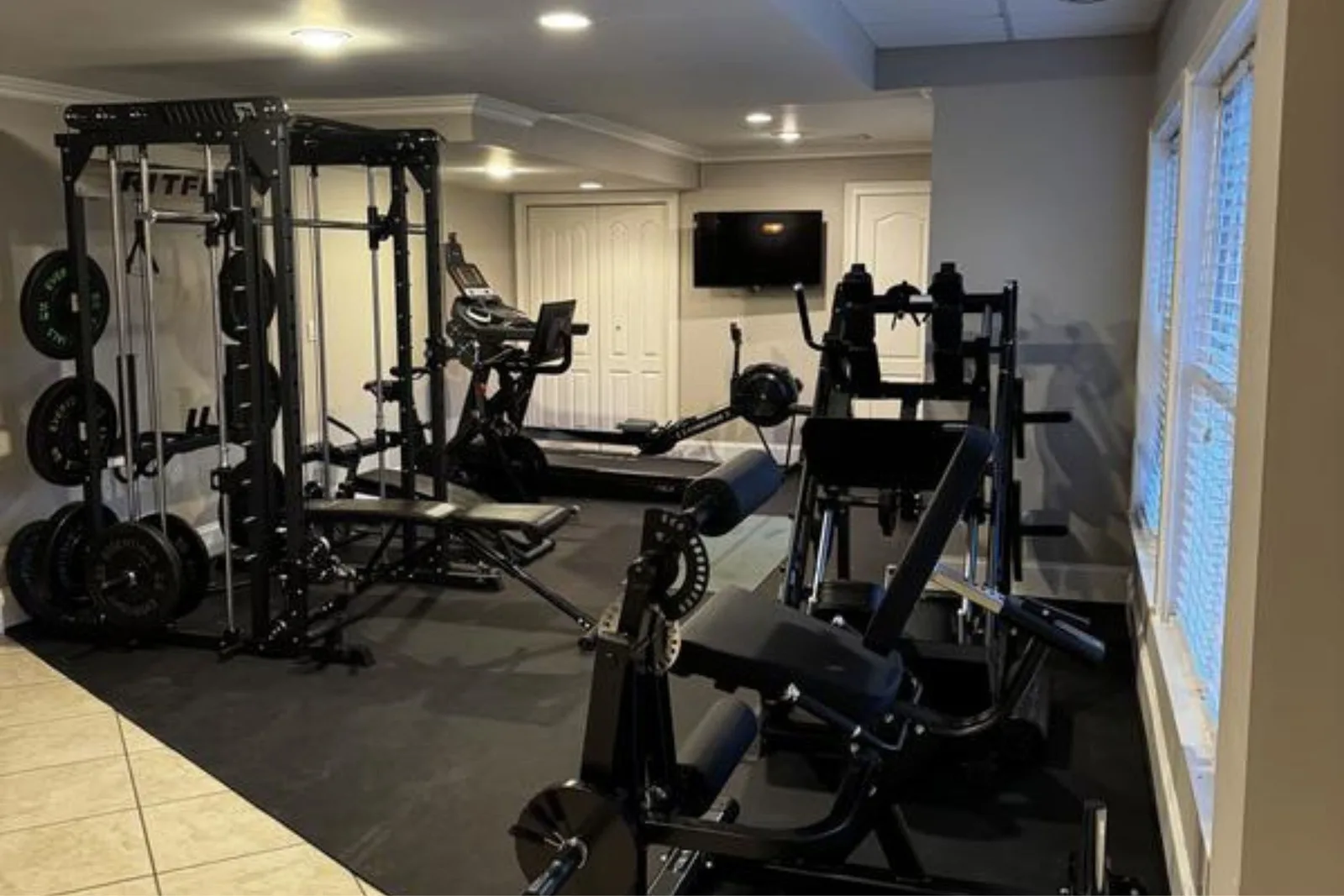 Black rubber gym flooring in a home gym featuring a squat rack, treadmill, and other workout equipment. The durable rubber matting protects floors and provides a stable, non-slip surface for exercise.