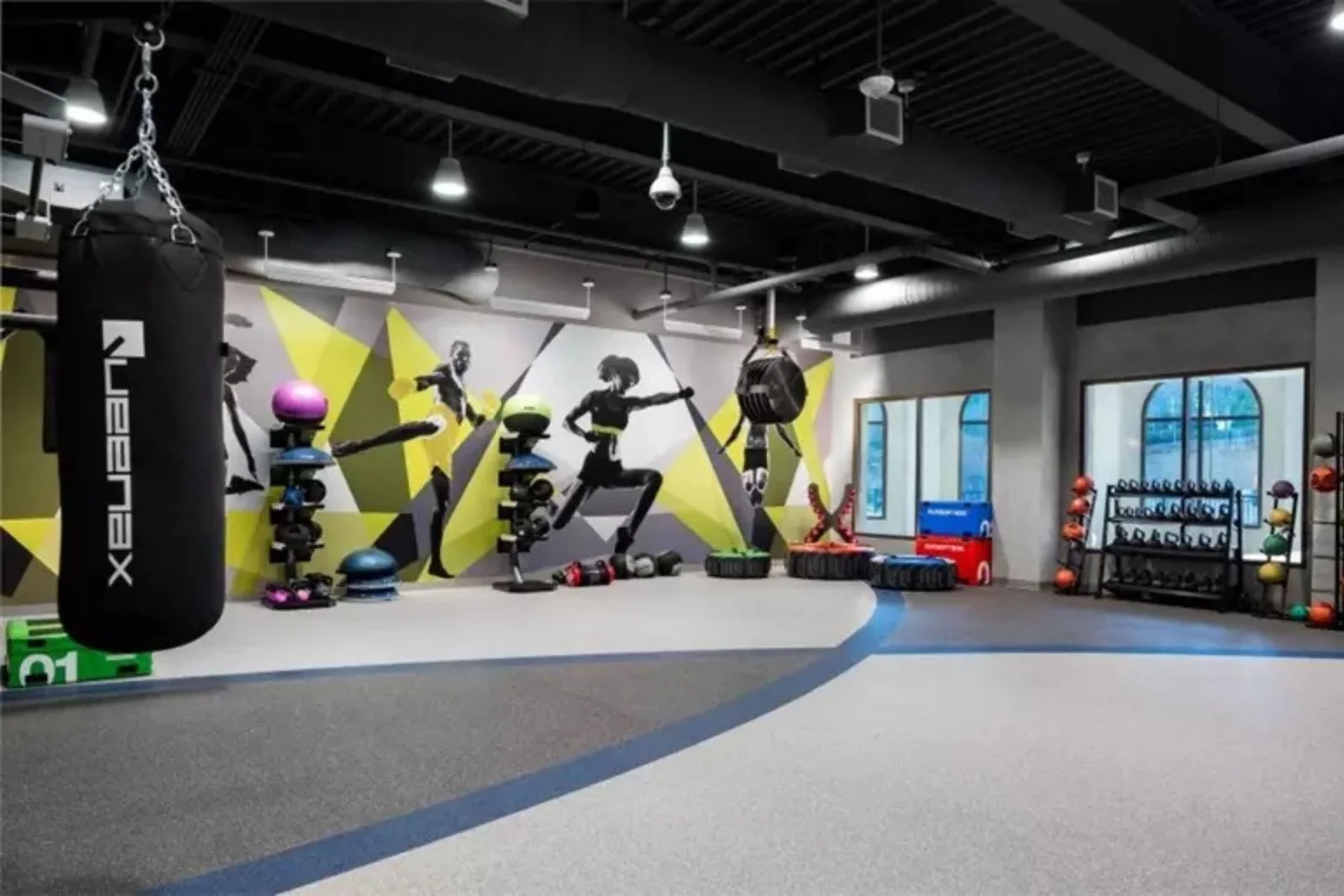 Rubber gym flooring in a commercial fitness studio, featuring a heavy punching bag, kettlebells, and colorful workout equipment. Durable interlocking rubber tiles provide a high-performance surface for intense training.