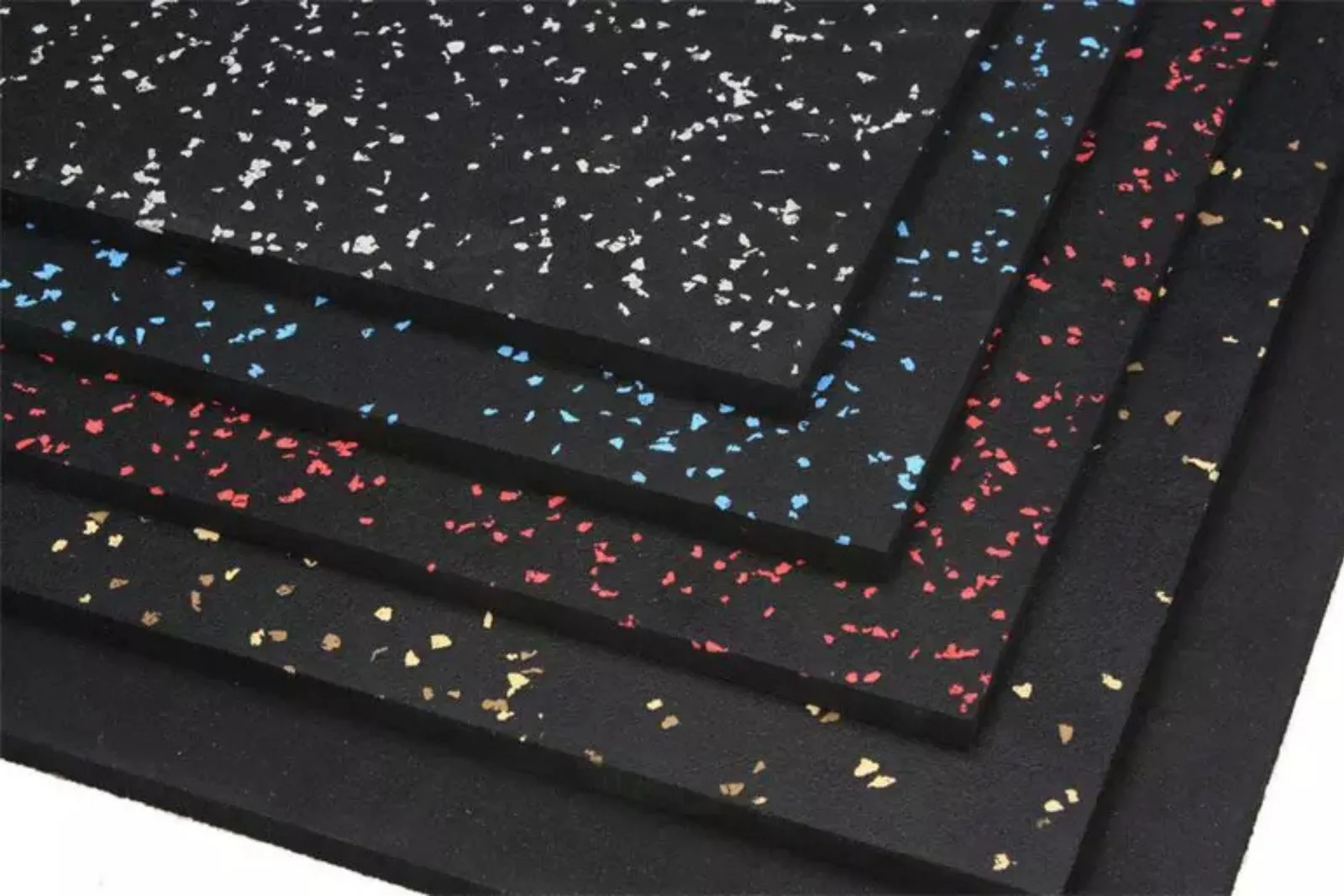 A close-up view of a stack of rubber gym flooring tiles in various colors. The different layers show speckled patterns in white, blue, red, and yellow, highlighting the variety of colorful gym mat options for a custom fitness space.