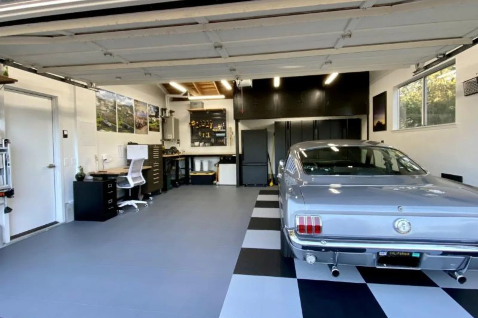 classic Ford Mustang is parked in a modern garage with black and grey interlocking floor tiles and a dedicated home office area.