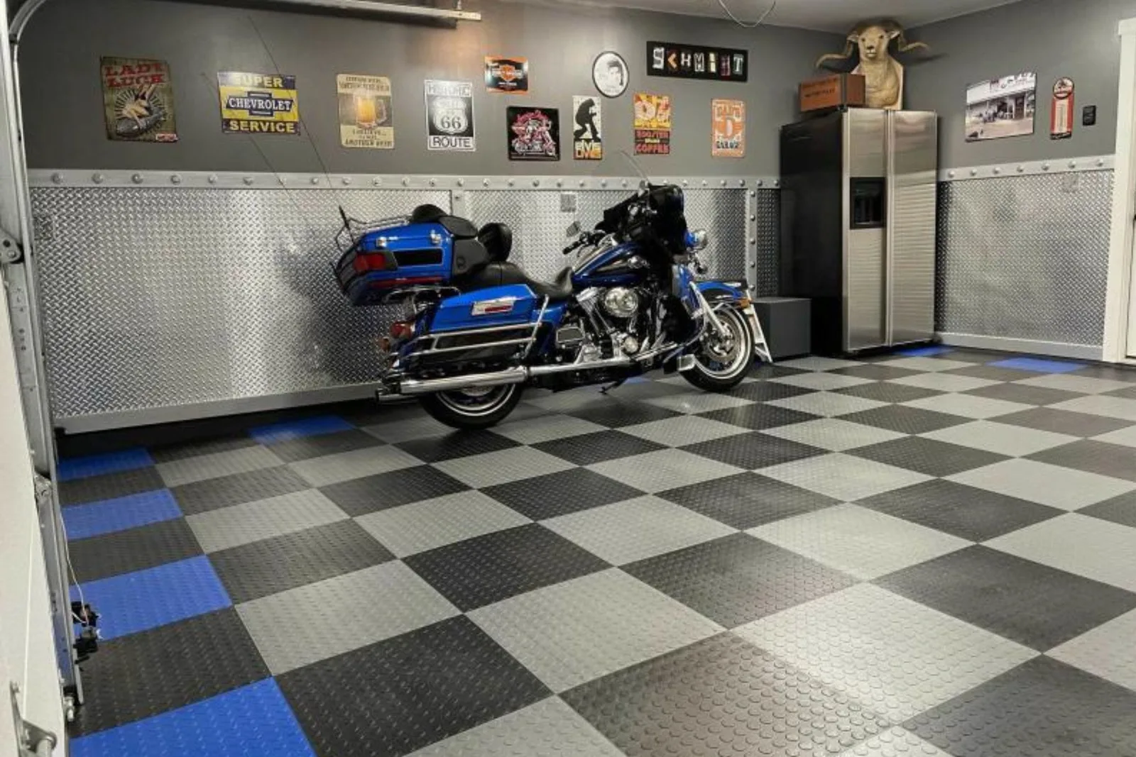 A motorcycle man cave featuring interlocking garage tiles in a black, gray, and blue checkerboard pattern with diamond plate walls.