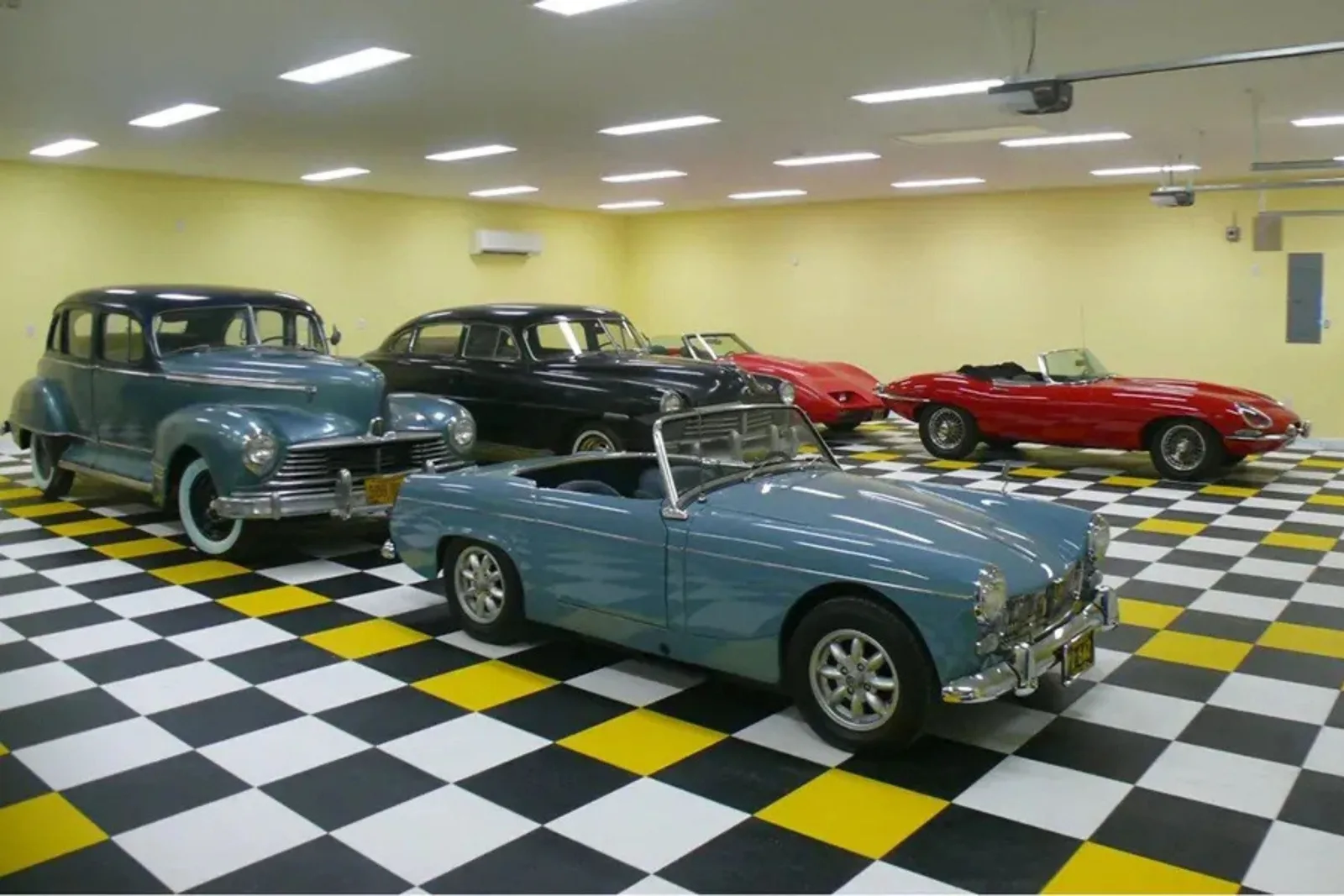 A classic car collection is on display in a garage with black, white, and yellow checkerboard floor tiles.