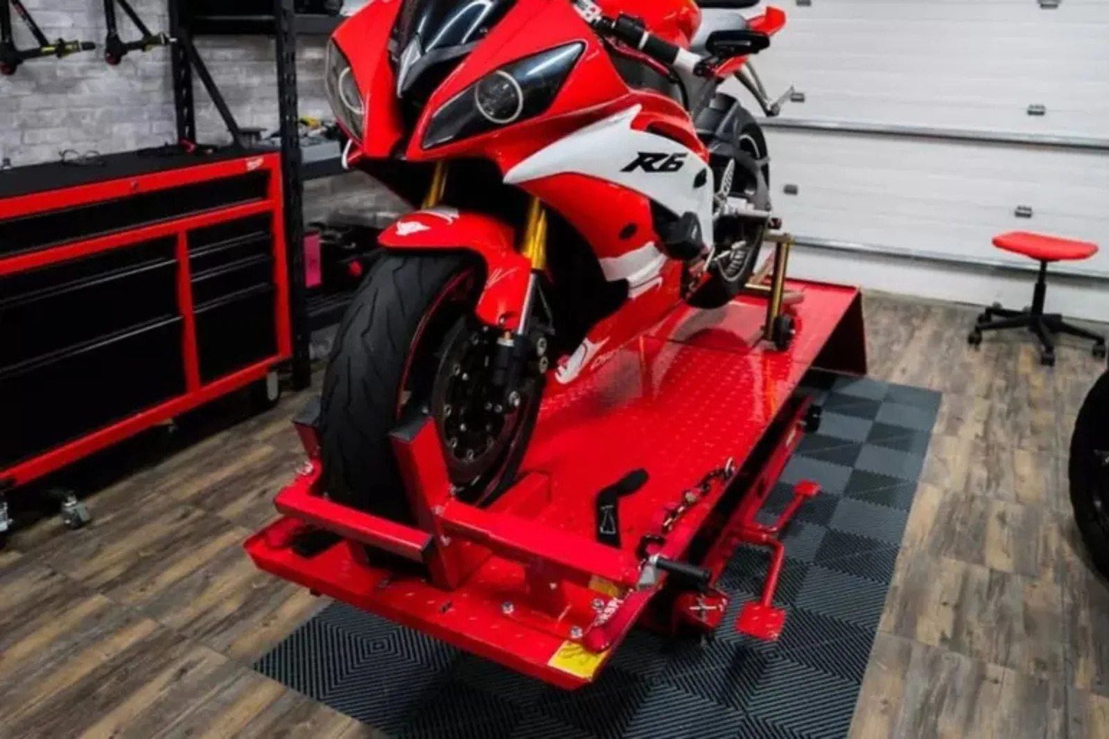 A sport motorcycle on a red hydraulic lift, showcasing durable grey checkerboard garage flooring in a motorcycle workshop.
