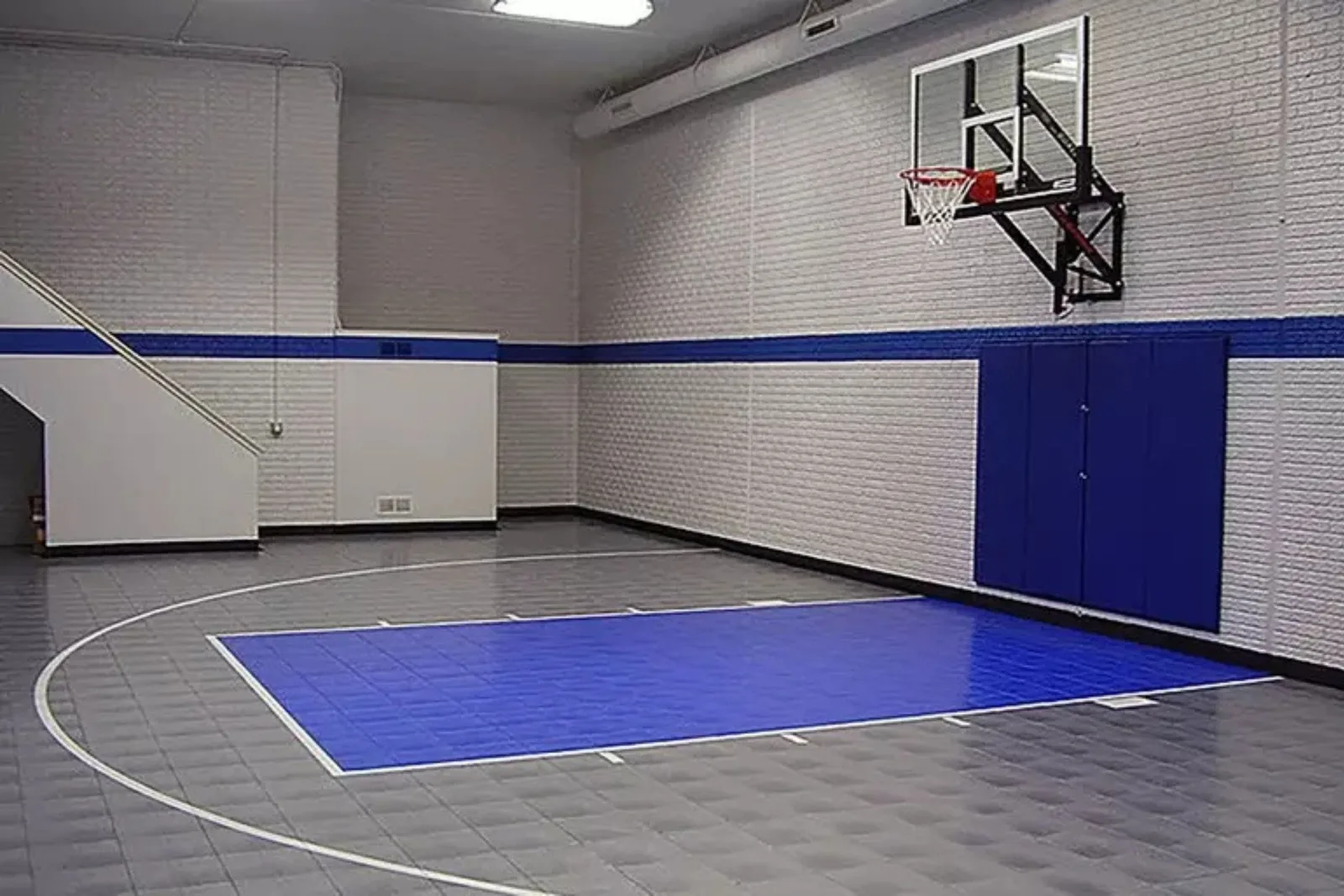 Indoor basketball court tiles in a gymnasium, creating a professional and low-maintenance sports flooring solution with a blue court and a grey perimeter.