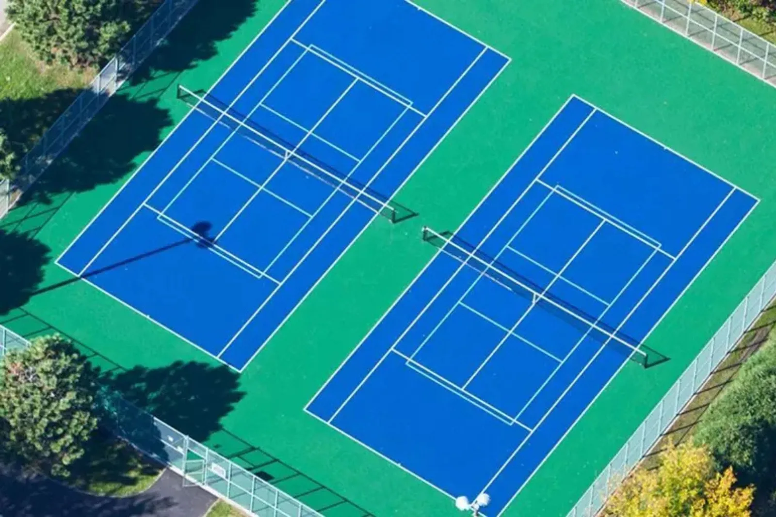 Interlocking outdoor tennis court tiles in vibrant blue and green, providing a durable, all-weather, and low-maintenance playing surface for two courts in a residential setting.