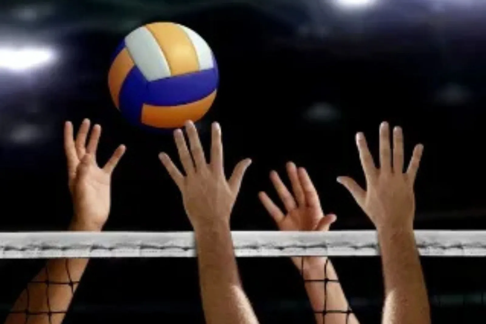 nterlocking volleyball court tiles provide a durable and high-performance flooring solution in a dimly lit indoor gymnasium, with players' hands visible as they block a ball over the net.