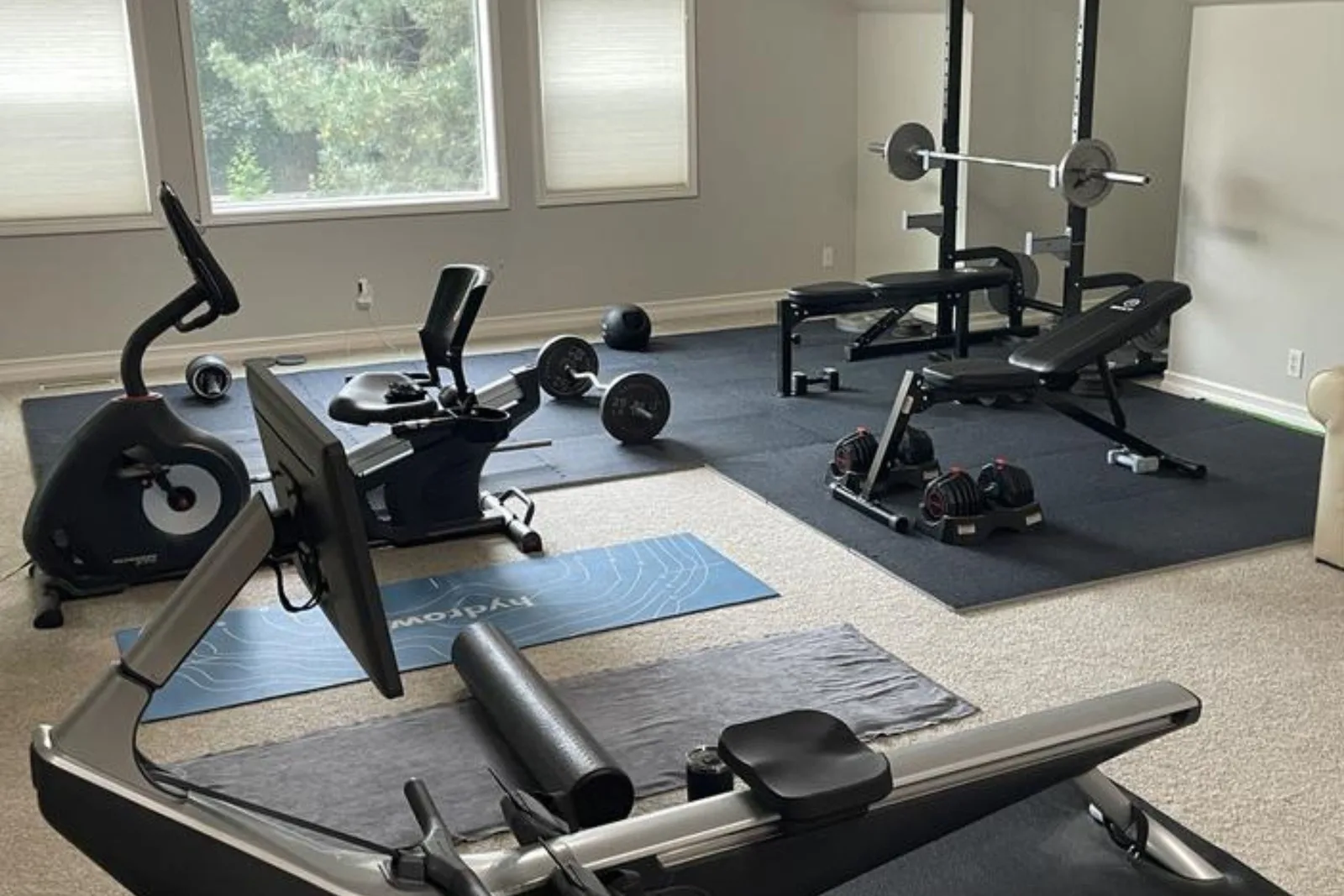 Home gym with durable black rubber interlocking gym floor tiles over a carpet, a protective and high-performance flooring solution for residential workout spaces.