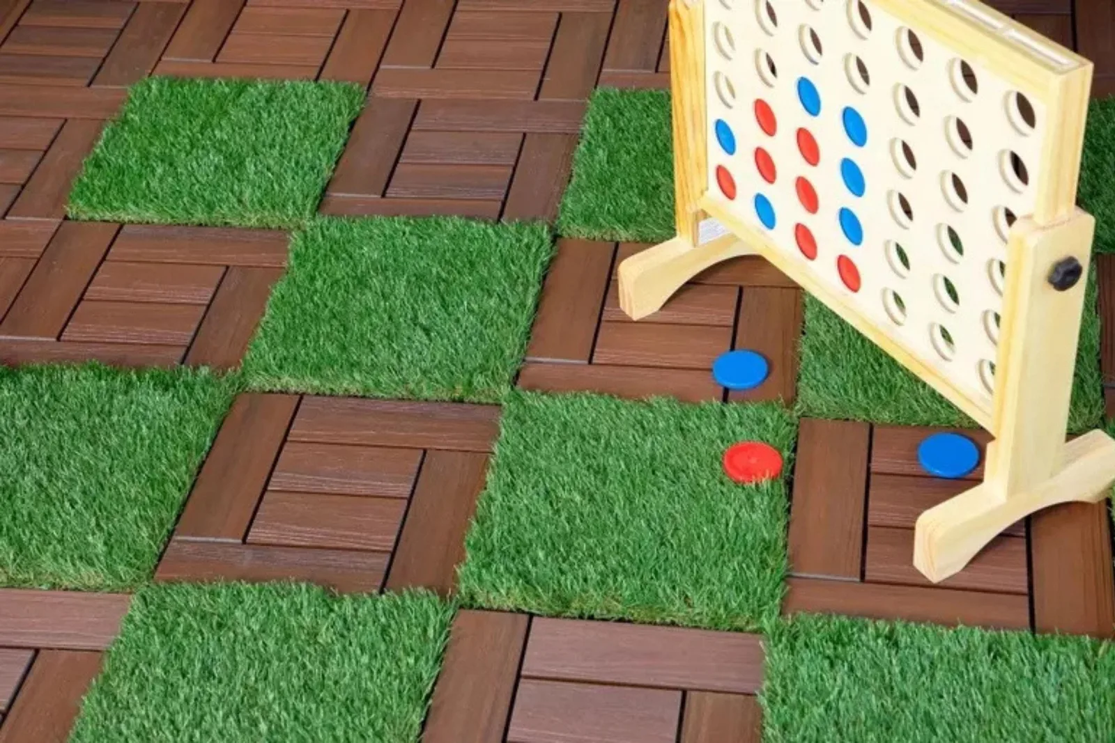 Composite deck tiles and artificial grass tiles create a unique, checkered outdoor flooring solution, providing a fun and low-maintenance patio surface for a game of giant Connect Four.