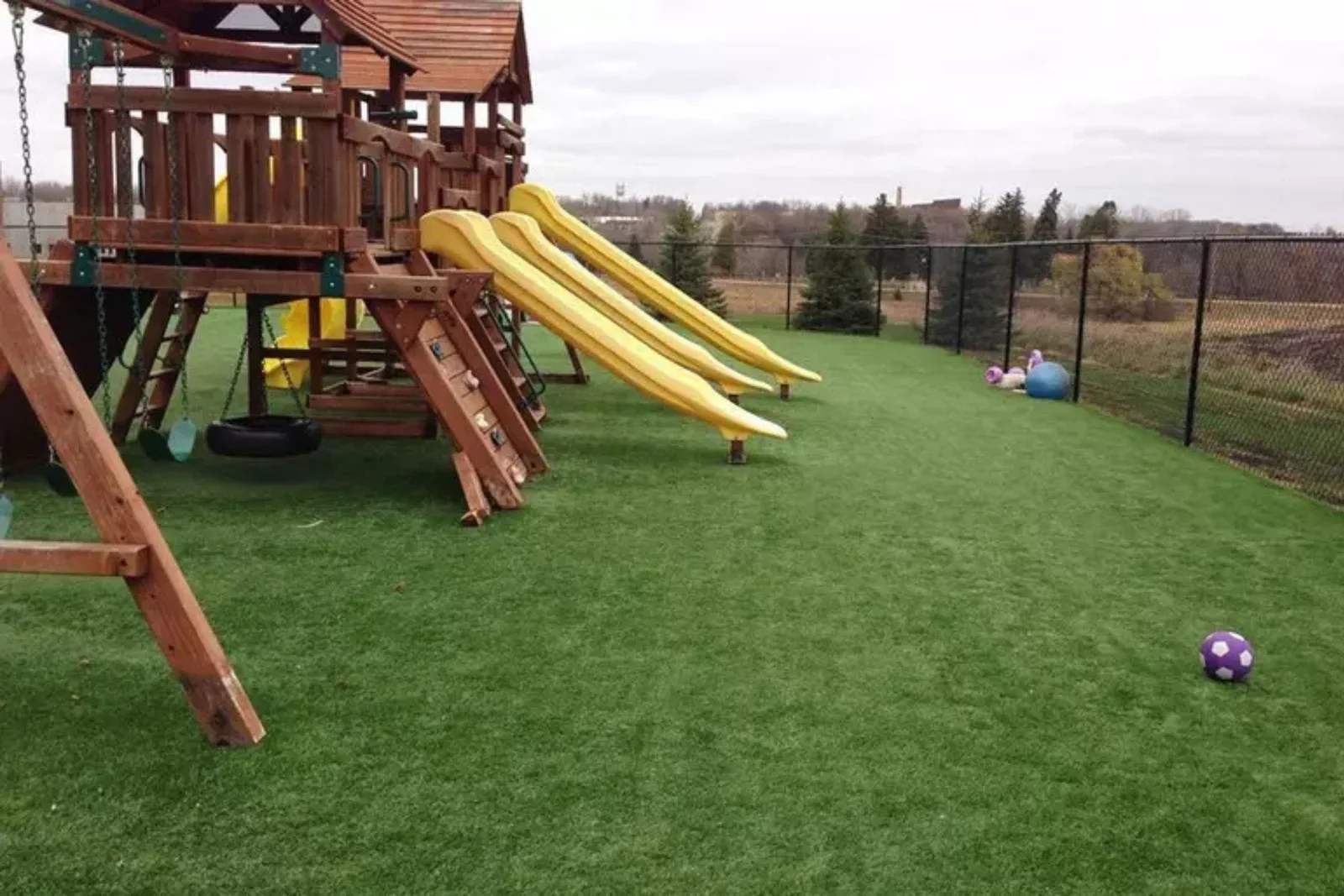 Artificial Grass Playground Turf Artificial grass playground turf in a backyard play area with a swingset and playhouse, creating a low-maintenance, safe, and clean play surface for kids.
