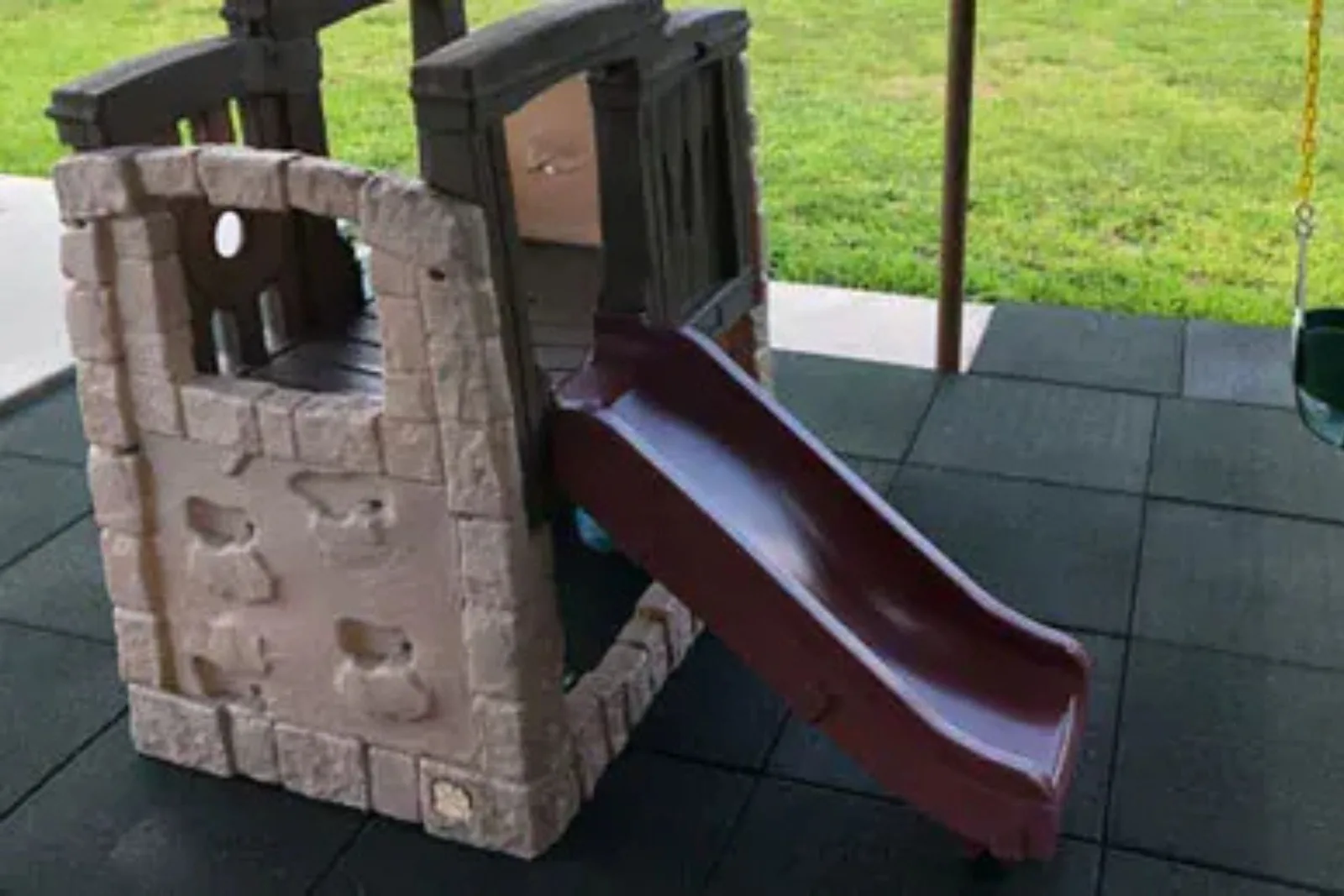 Rubber playground tiles in a black finish provide a cushioned and safe surface around a kids' playhouse with a slide.
