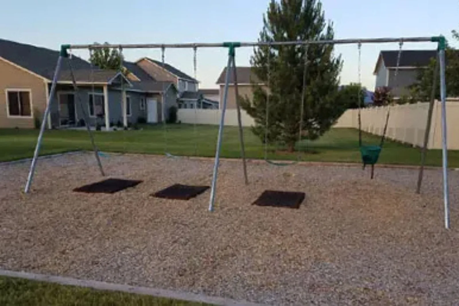Black rubber playground swing mats are used under a swing set in a residential backyard, providing extra shock absorption and safety for children in high-traffic areas.