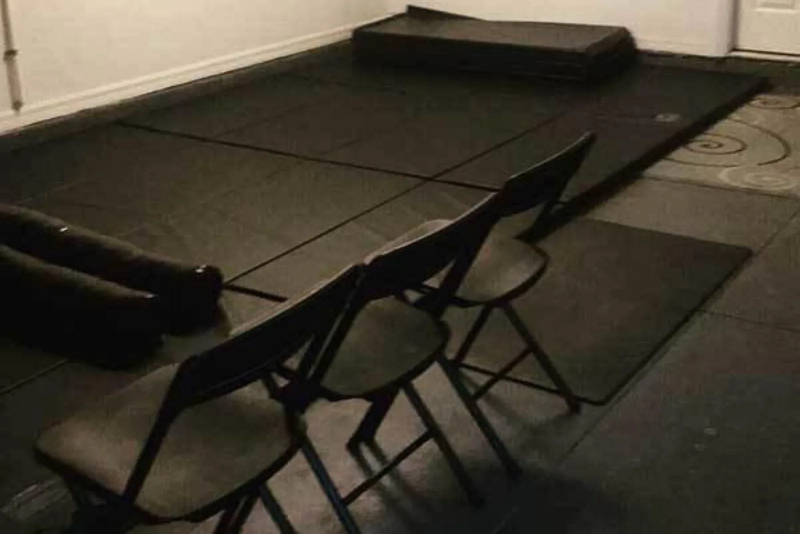 Black martial arts mats create a safe and versatile folding foam panel mat surface for home training, with chairs and equipment nearby.