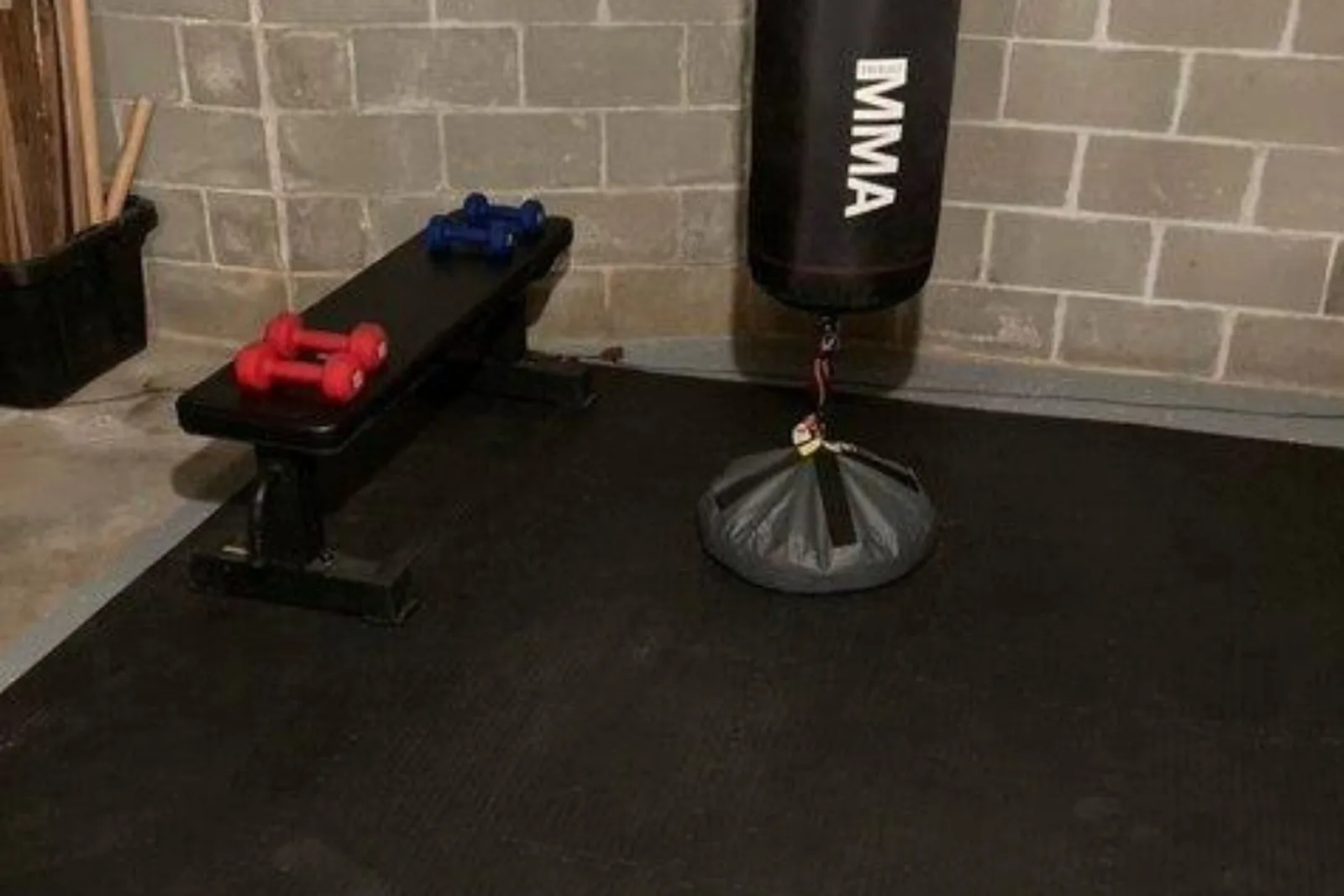 Tatami foam tiles create a durable, interlocking black surface for a home gym, providing cushioned martial arts mats for a punching bag, weight bench, and training area.