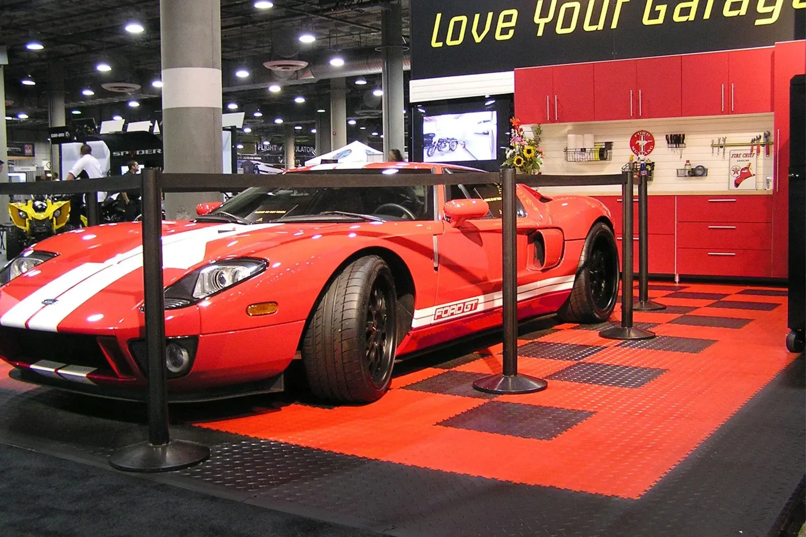 Interlocking PVC garage floor tiles in a red and black checkered pattern, creating a durable and stylish display floor for a red Ford GT at a trade show or auto show