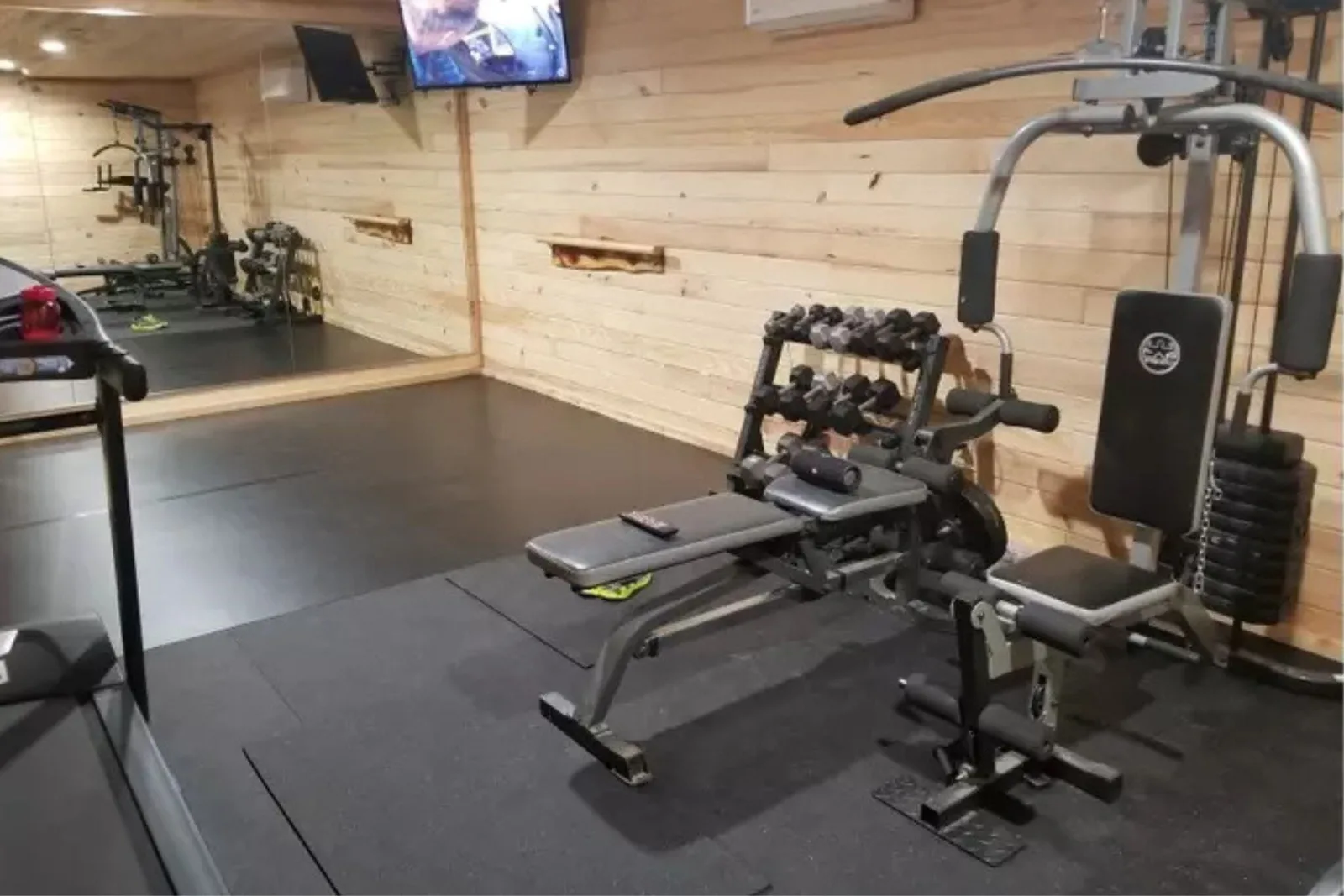 Durable black rubber gym flooring Home gym with light wood paneling and durable black rubber gym flooring, providing a supportive and resilient surface for weight training equipment.
