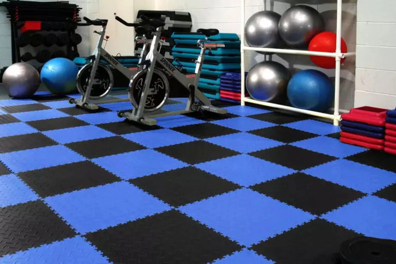 Durable interlocking foam floor tiles Home gym with durable black and blue interlocking foam floor tiles, providing a colorful and shock-absorbing surface for exercise equipment.