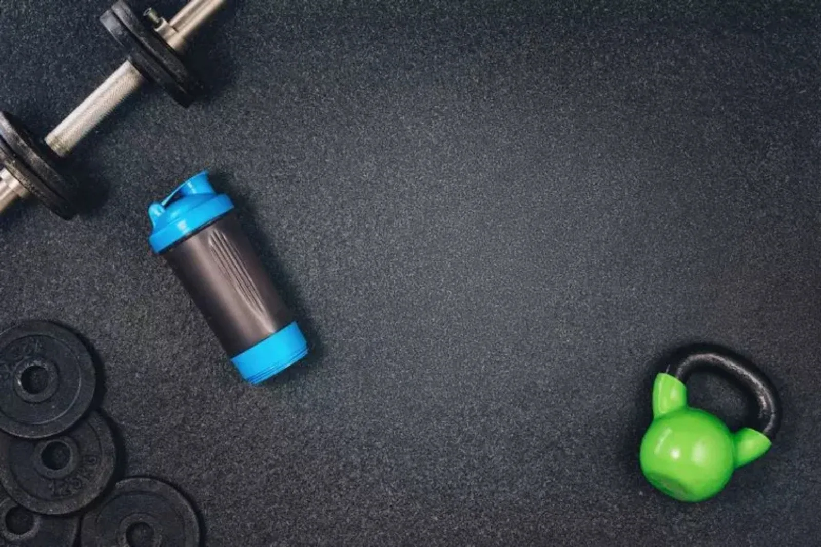 Durable black rubber gym flooring Overhead view of a barbell, weight plates, a shaker bottle, and a kettlebell resting on durable black rubber gym flooring, providing a protective workout surface.